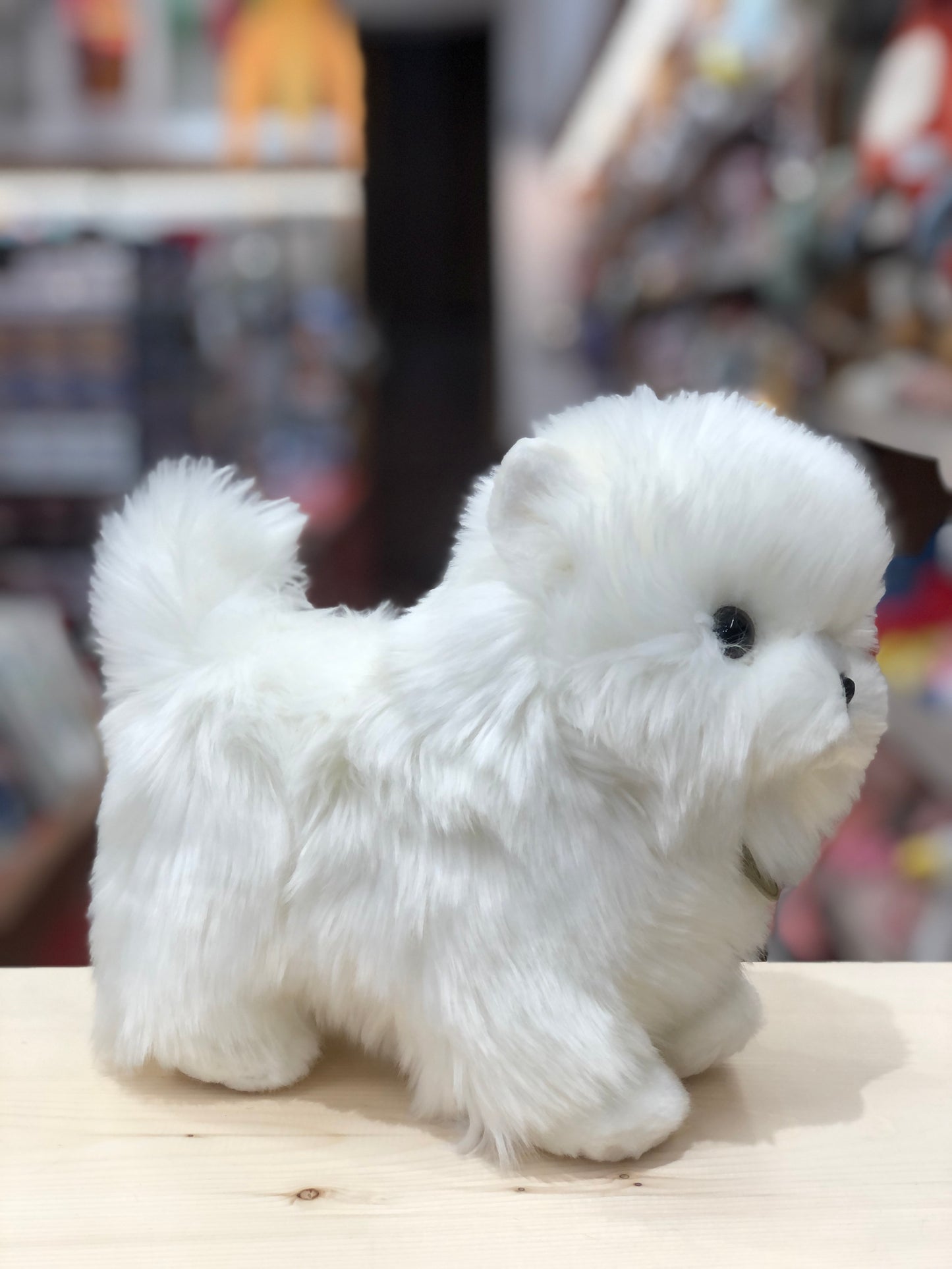 Adorable white Aurora Miyoni Tots Pompom Pup plush toy, 9 inches tall, standing on wooden surface in toy store setting
