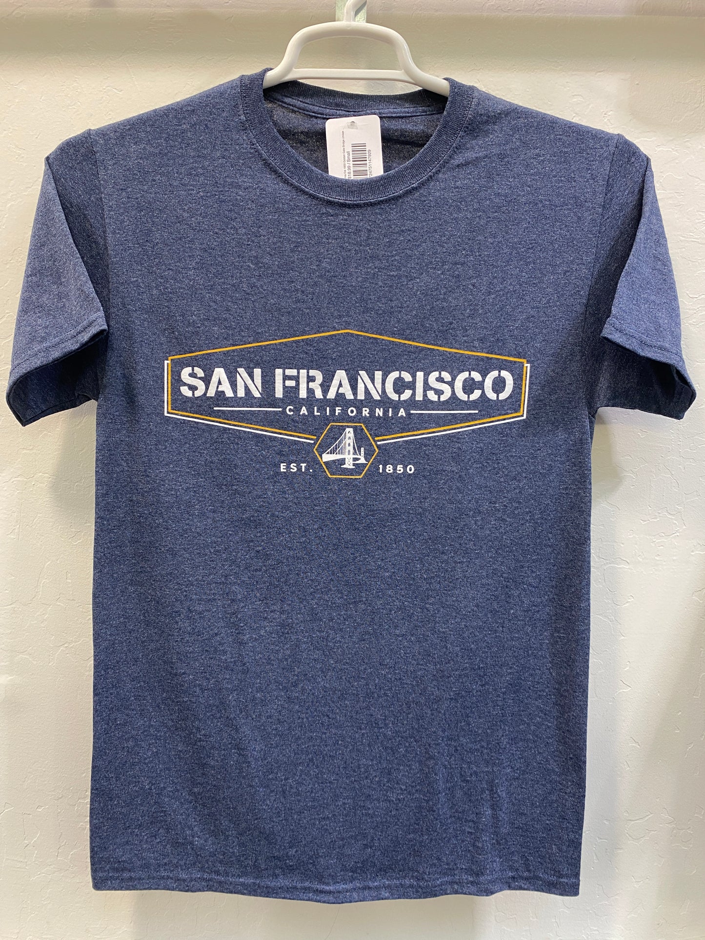 Front view of a blue heathered crewneck t-shirt hanging on a white plastic hanger against a white wall. The shirt features a sharp, screen-printed graphic across the chest with a gold hexagonal frame surrounding the bold text "SAN FRANCISCO CALIFORNIA". Below the main text, a circular emblem highlights a white silhouette of the Golden Gate Bridge, flanked by the founding year "EST. 1850".