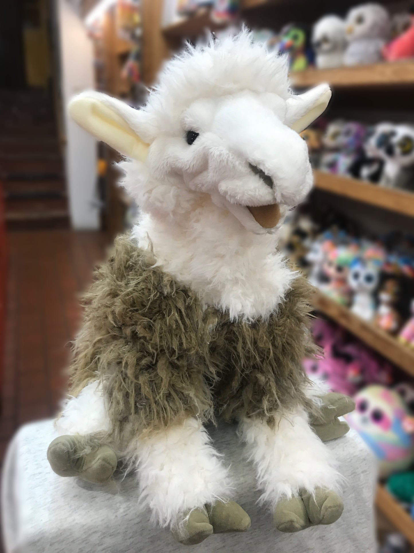 Soft, cuddly Folkmanis alpaca puppet with white fluffy head and brown woolly body, sitting on display in toy store