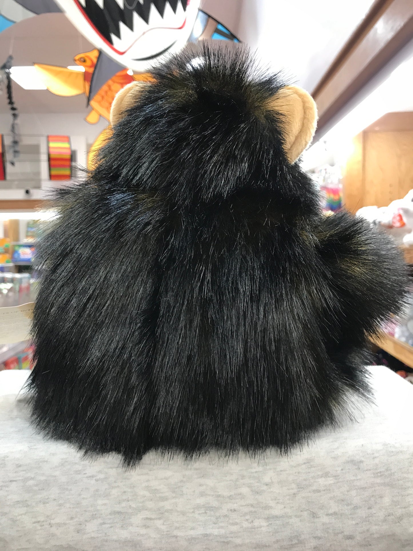 Fluffy black baby chimpanzee puppet with tan ears, viewed from behind in a toy store setting