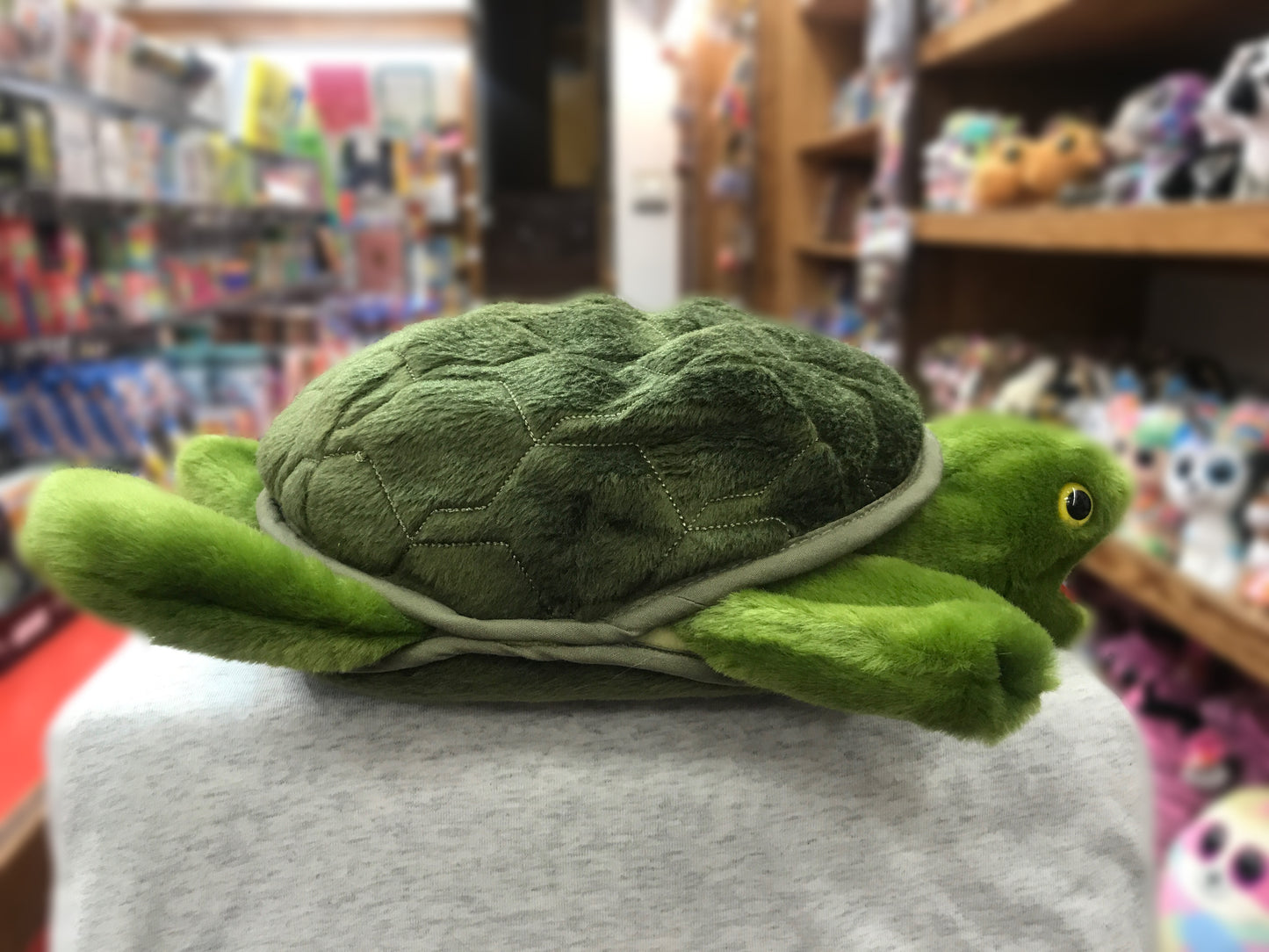 Plush green Folkmanis turtle puppet with movable features displayed in toy store, showcasing detailed shell and bright eye