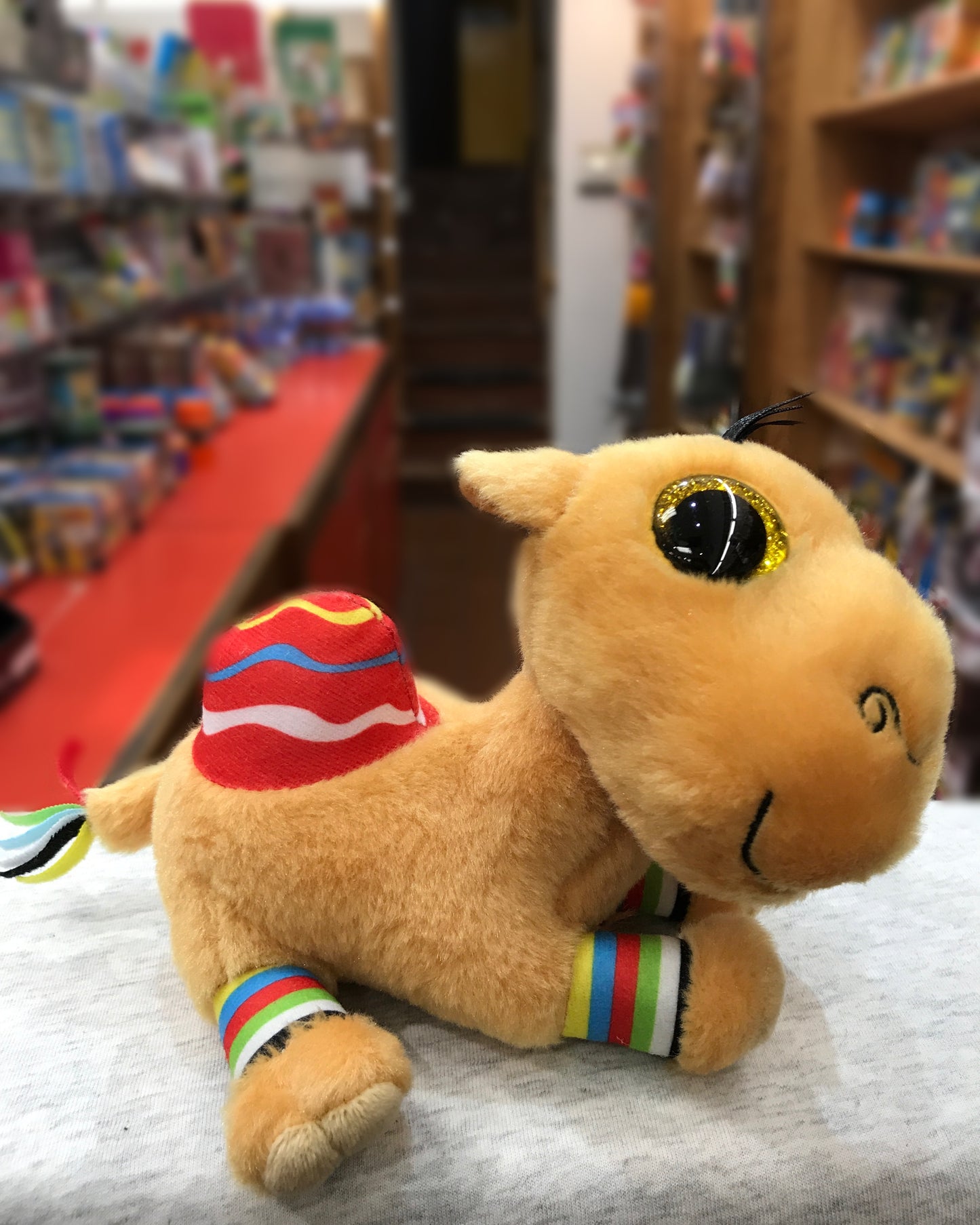 Adorable Ty Beanie Boo Jamal Camel plush toy with big sparkly eyes and colorful accents, displayed in a toy store setting