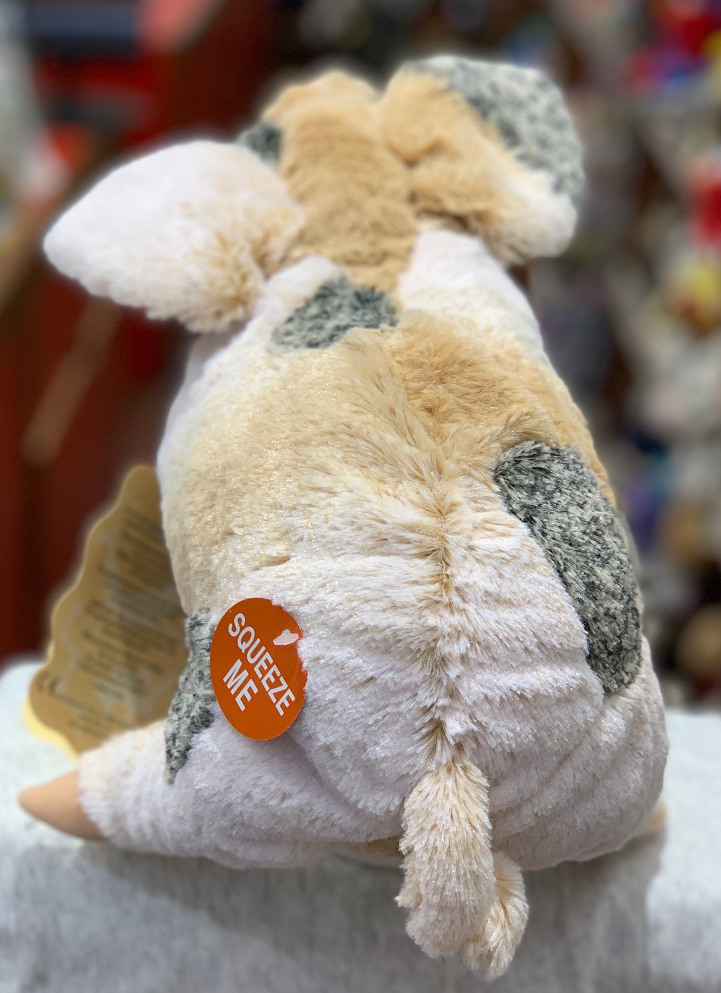 Folkmanis grunting pig puppet with soft plush fur, grey patches, curly tail, and orange "Squeeze Me" tag on its side