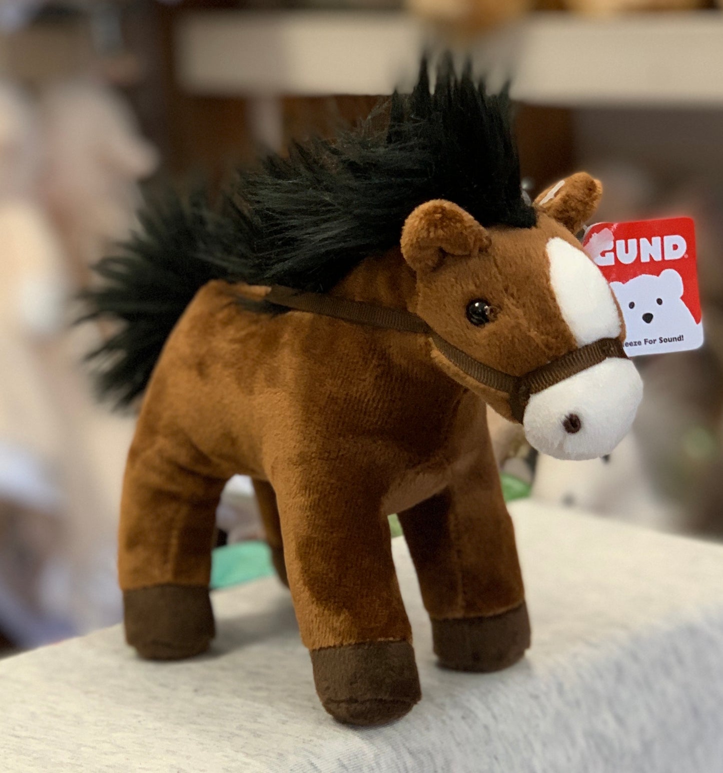 Gund brown plush horse toy with black mane, white muzzle, and sound feature, displayed on table with attached tag