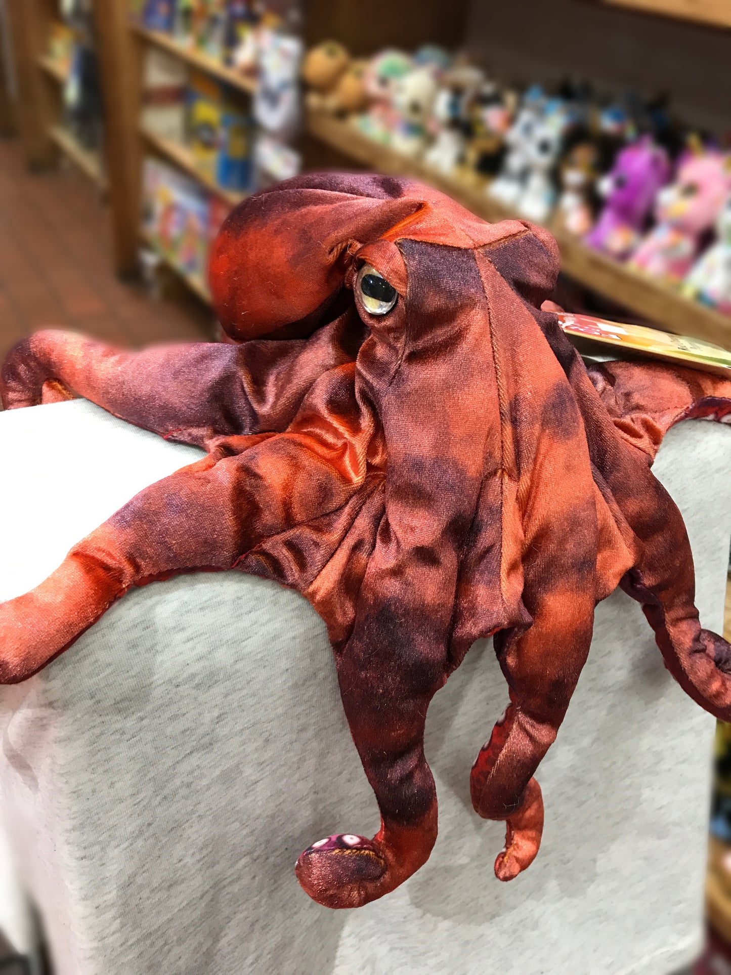 Lifelike red octopus puppet with movable arms and realistic eye, displayed in toy store setting
