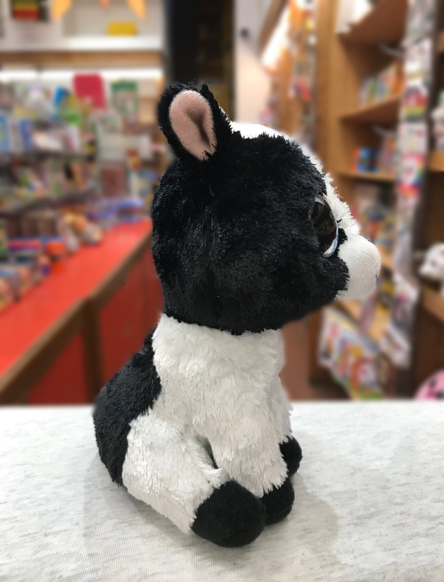 Adorable Ty Beanie Boo Butter Cow plush toy, black and white, sitting on display in a toy store with bookshelves in background