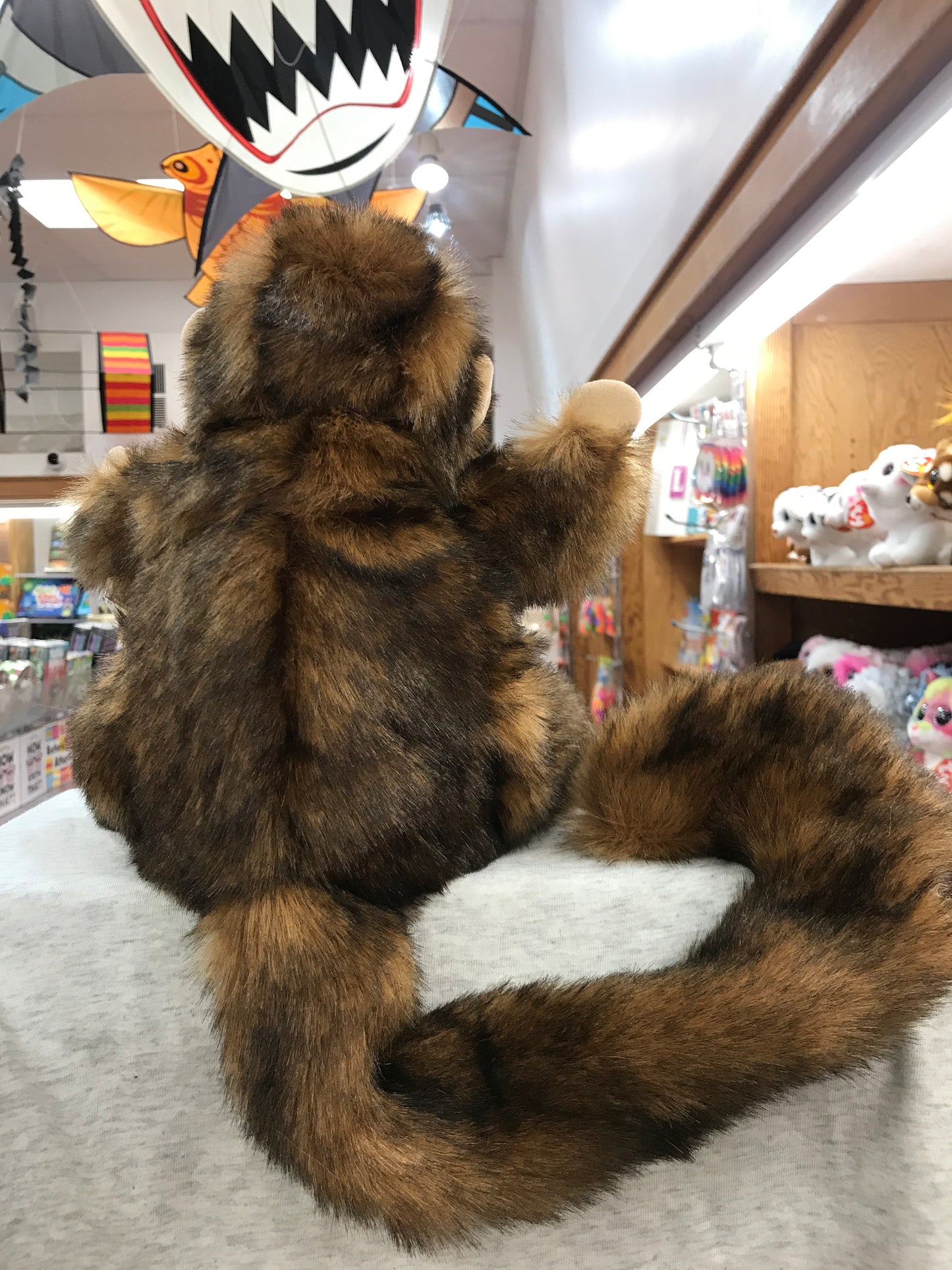 Folkmanis monkey puppet with brown fur, sitting on display in toy store, arms raised playfully