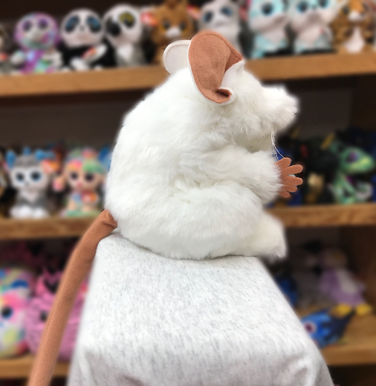 Folkmanis white mouse puppet with movable arms and big ears, sitting alert among colorful toys on shelves