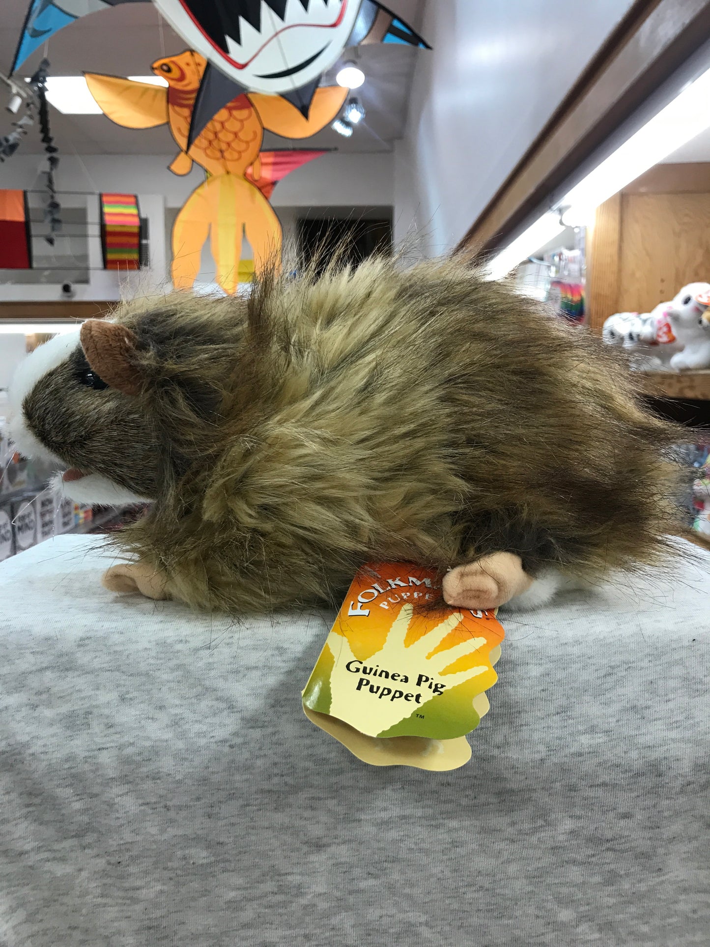 Folkmanis Guinea Pig Puppet on display, fuzzy and lifelike, with product tag visible in toy store setting