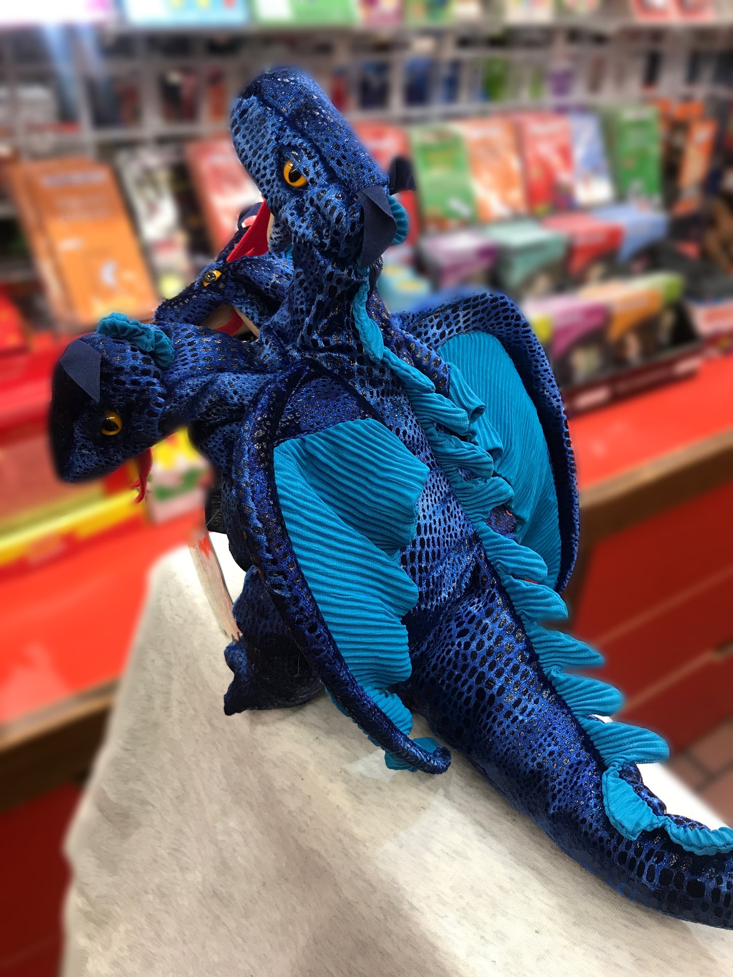 Folkmanis three-headed dragon puppet with blue scales and wings, displayed in a toy store setting