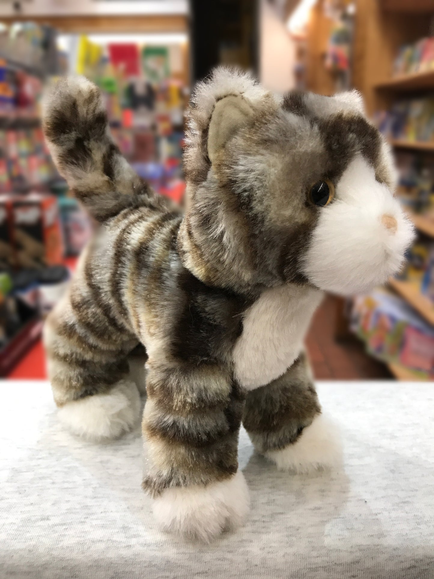 Soft and lifelike Douglas Zigby gray striped cat plush toy standing alert with white markings and golden eyes in toy store