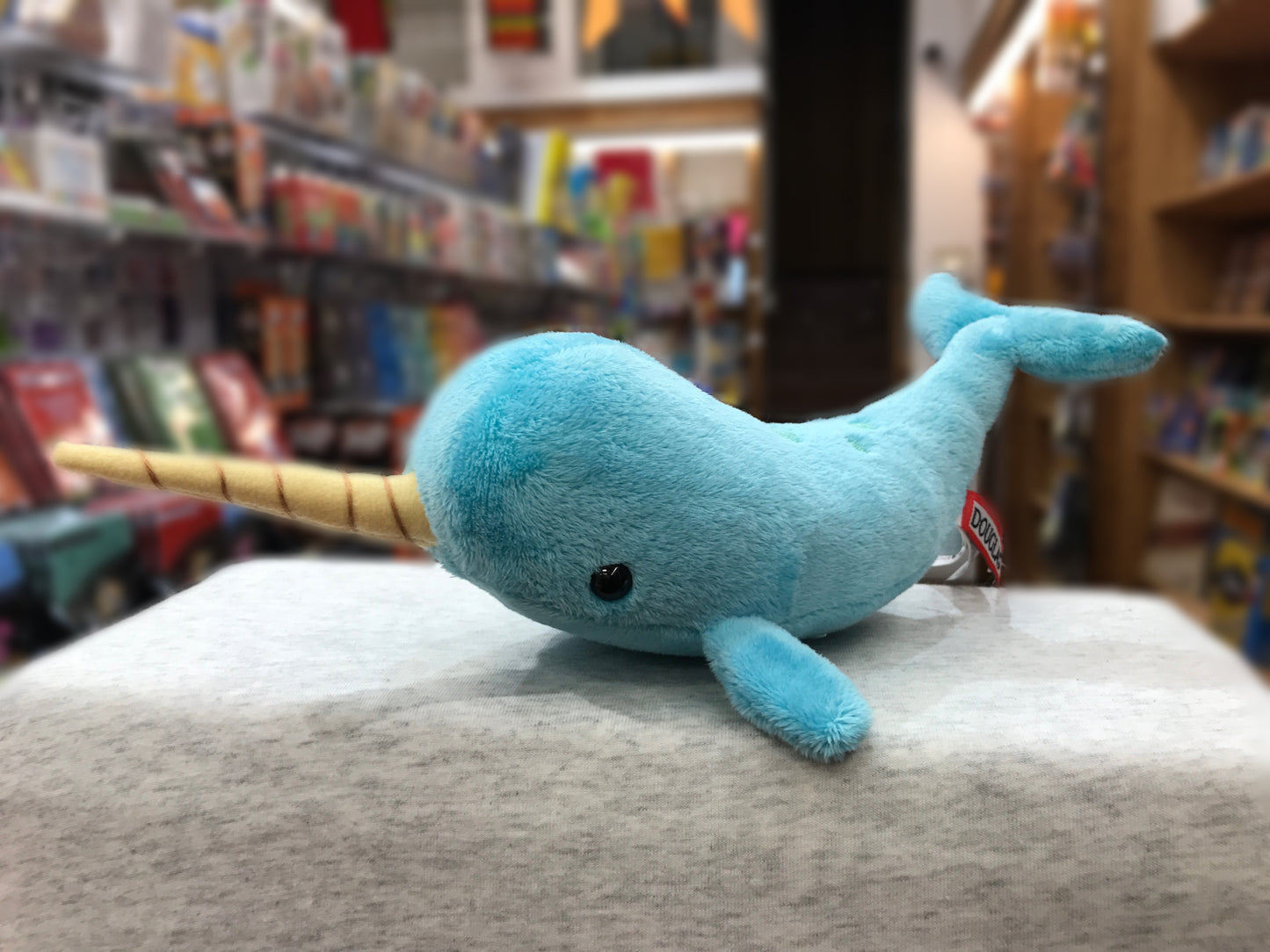 Soft turquoise narwhal plush toy with spiraled tusk on display in toy store, showcasing cuddly sea creature stuffed animal