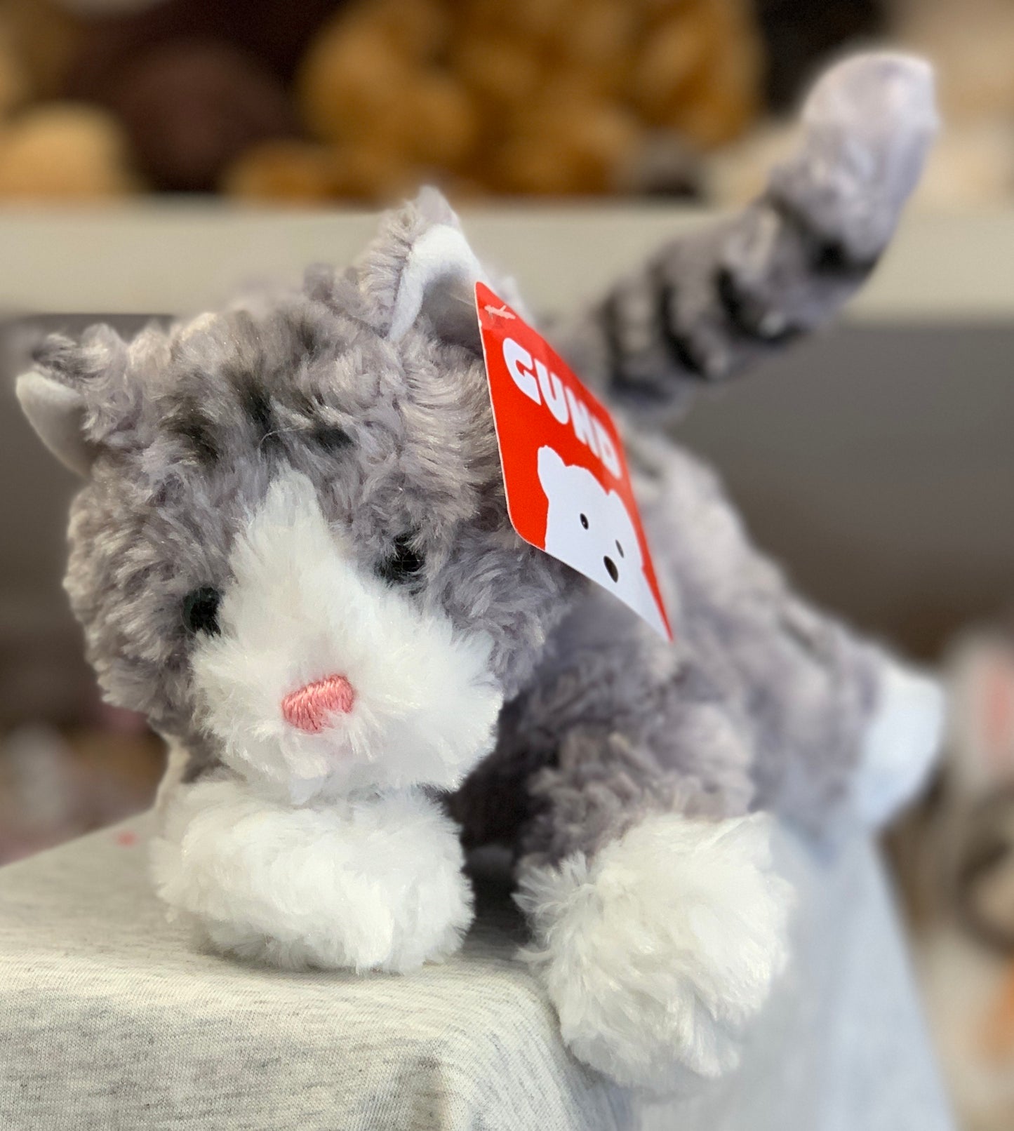 Gund Bootsie grey cat plush toy with white paws and pink nose, featuring red Gund tag, on display