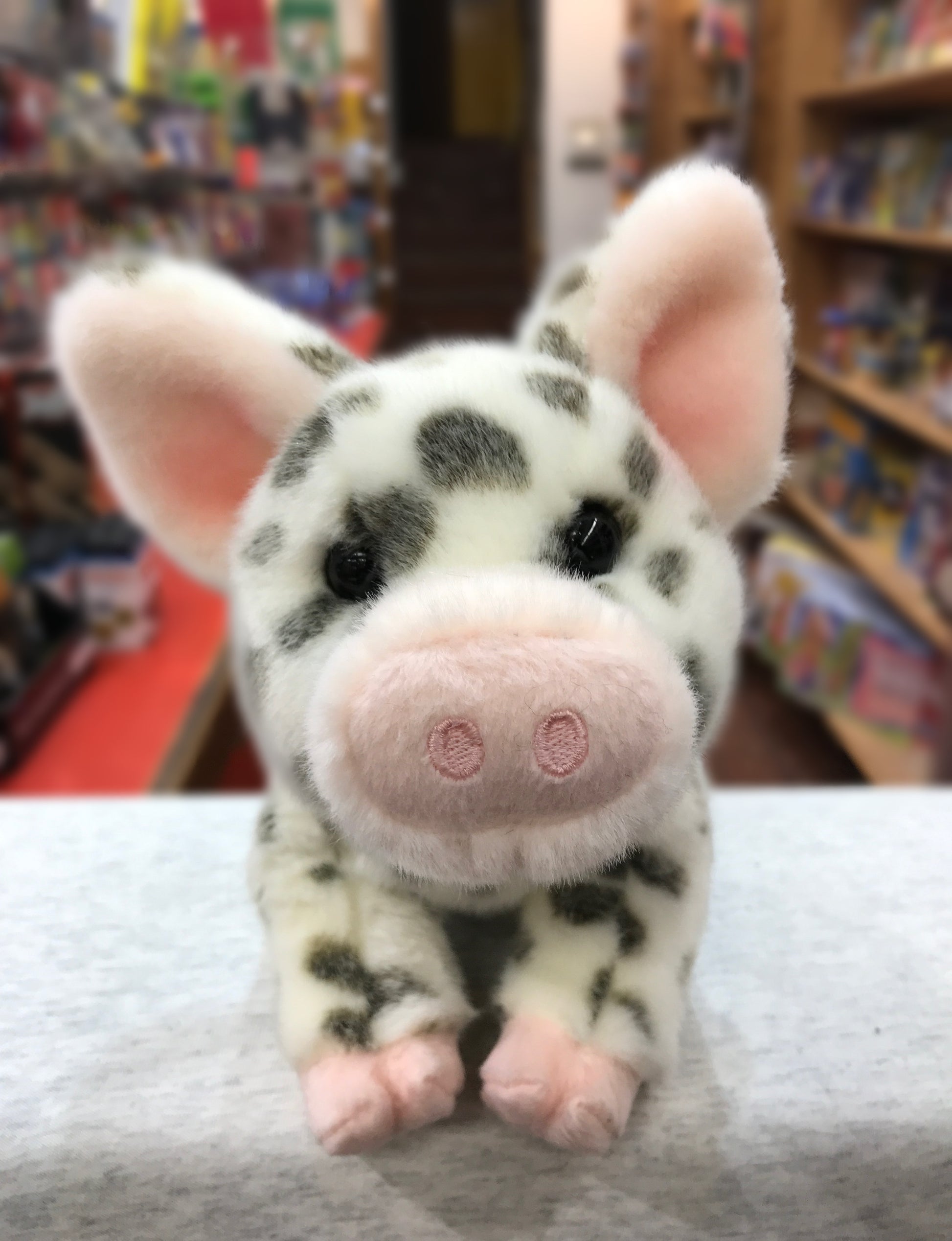 Cuddly spotted pig plush toy with pink ears and snout, sitting on display in toy store