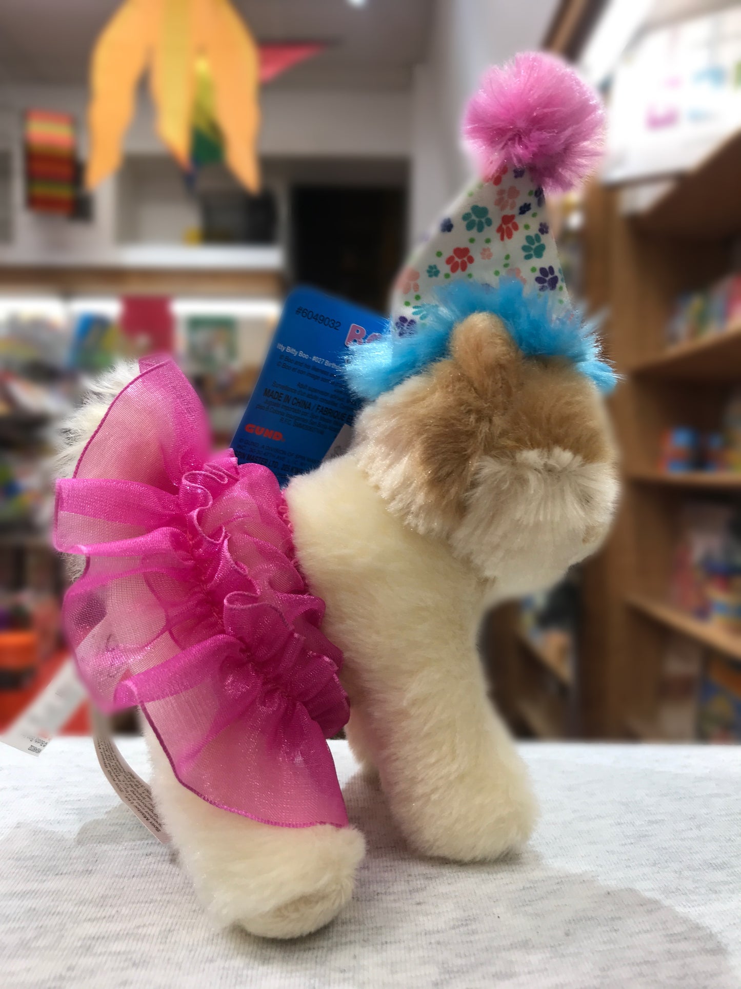 Gund Itty Bitty Boo plush dog in pink tutu and colorful birthday hat, displayed in store setting