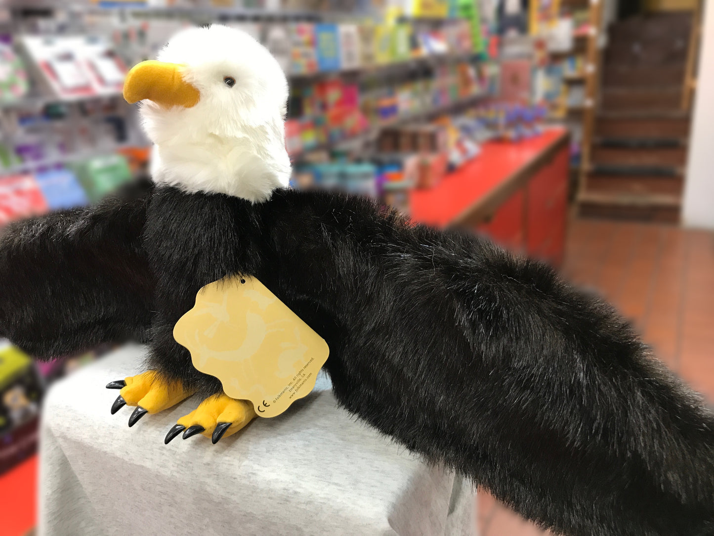 Realistic Folkmanis bald eagle puppet with white head, black body, and yellow beak and talons, displayed in toy store
