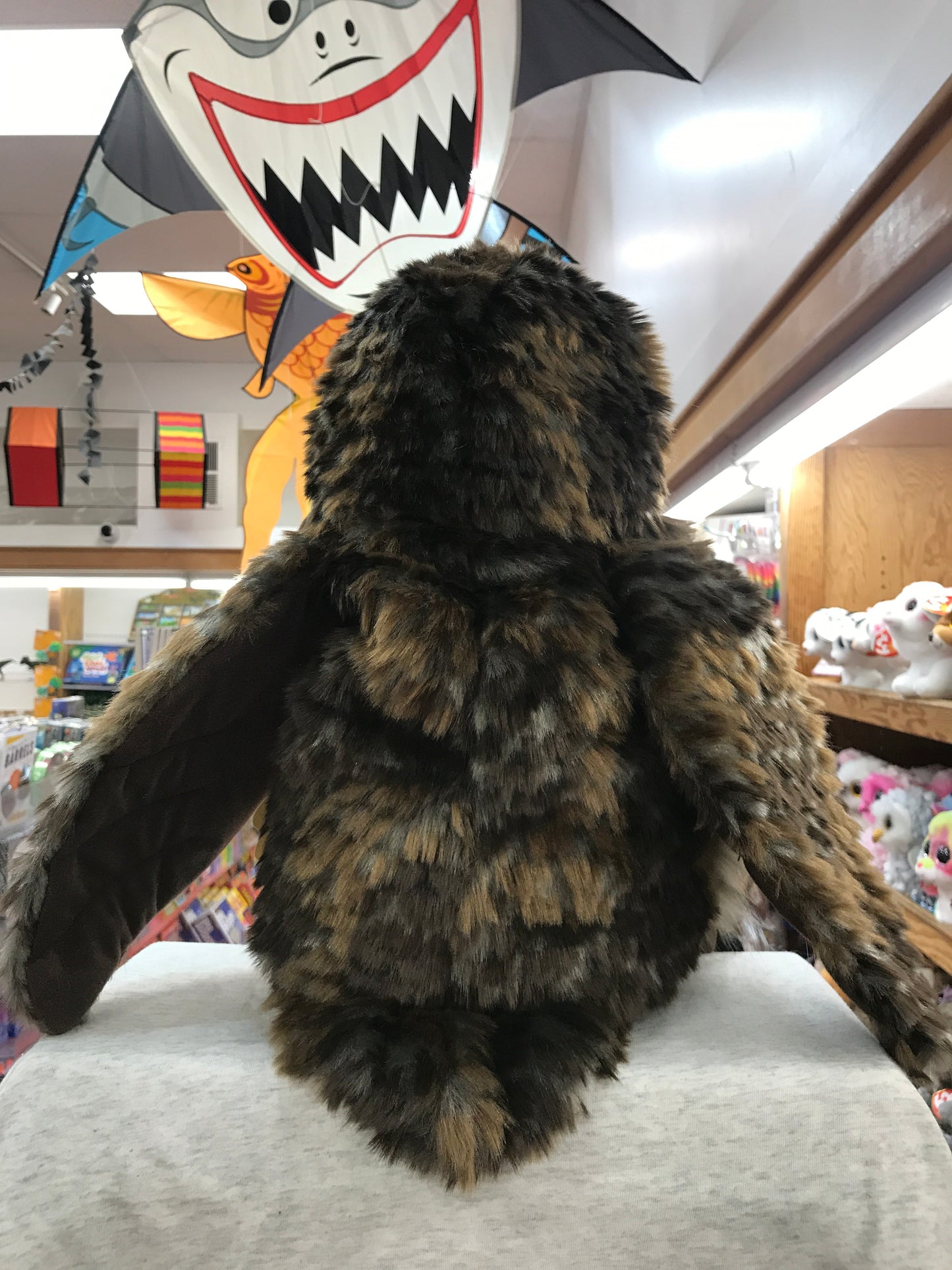 Realistic Folkmanis hooting owl puppet with fluffy plumage in toy store, surrounded by colorful decorations and other toys