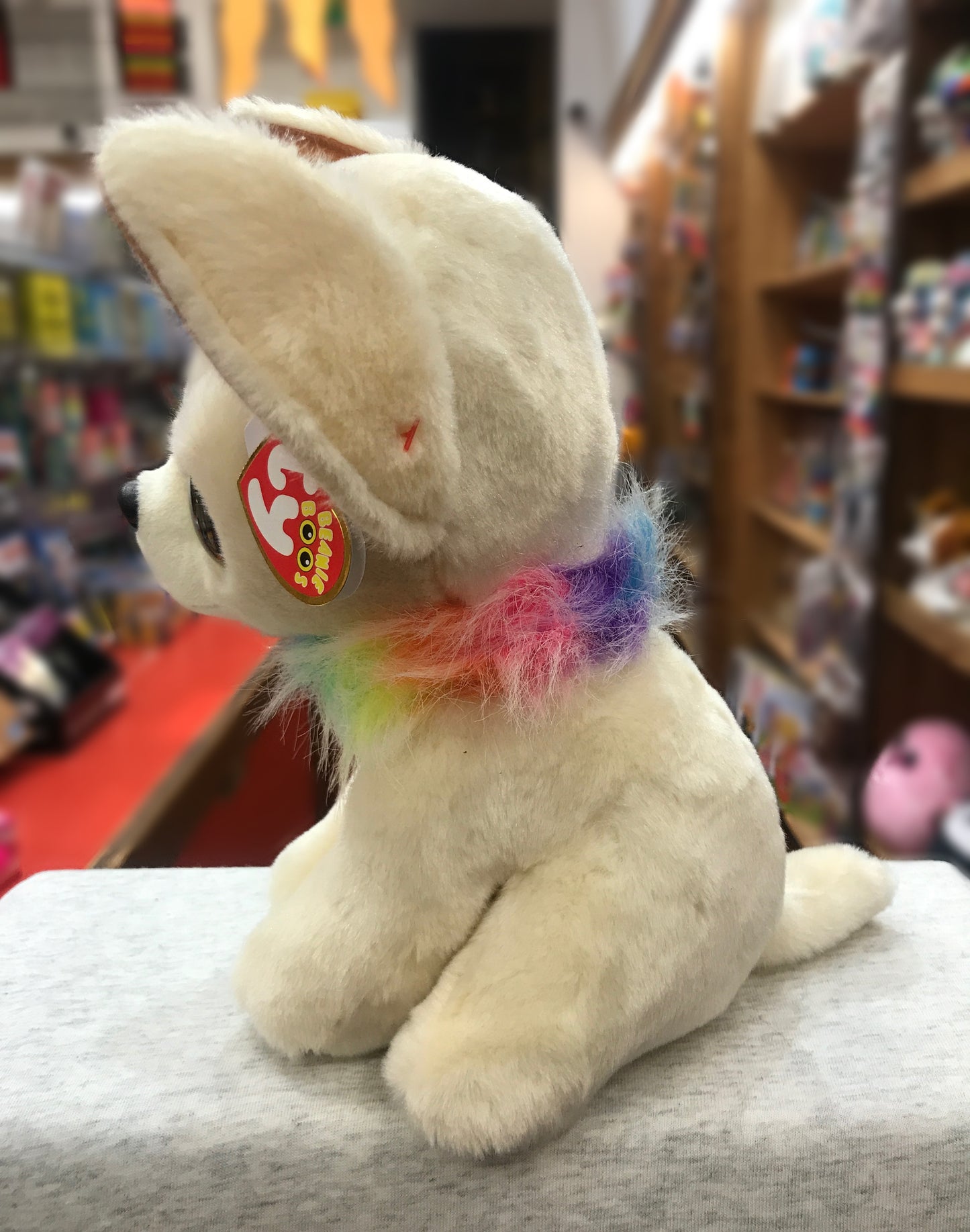Ty Beanie Boo Chewey Chihuahua plush with soft cream fur and colorful rainbow collar, sitting on display in toy store
