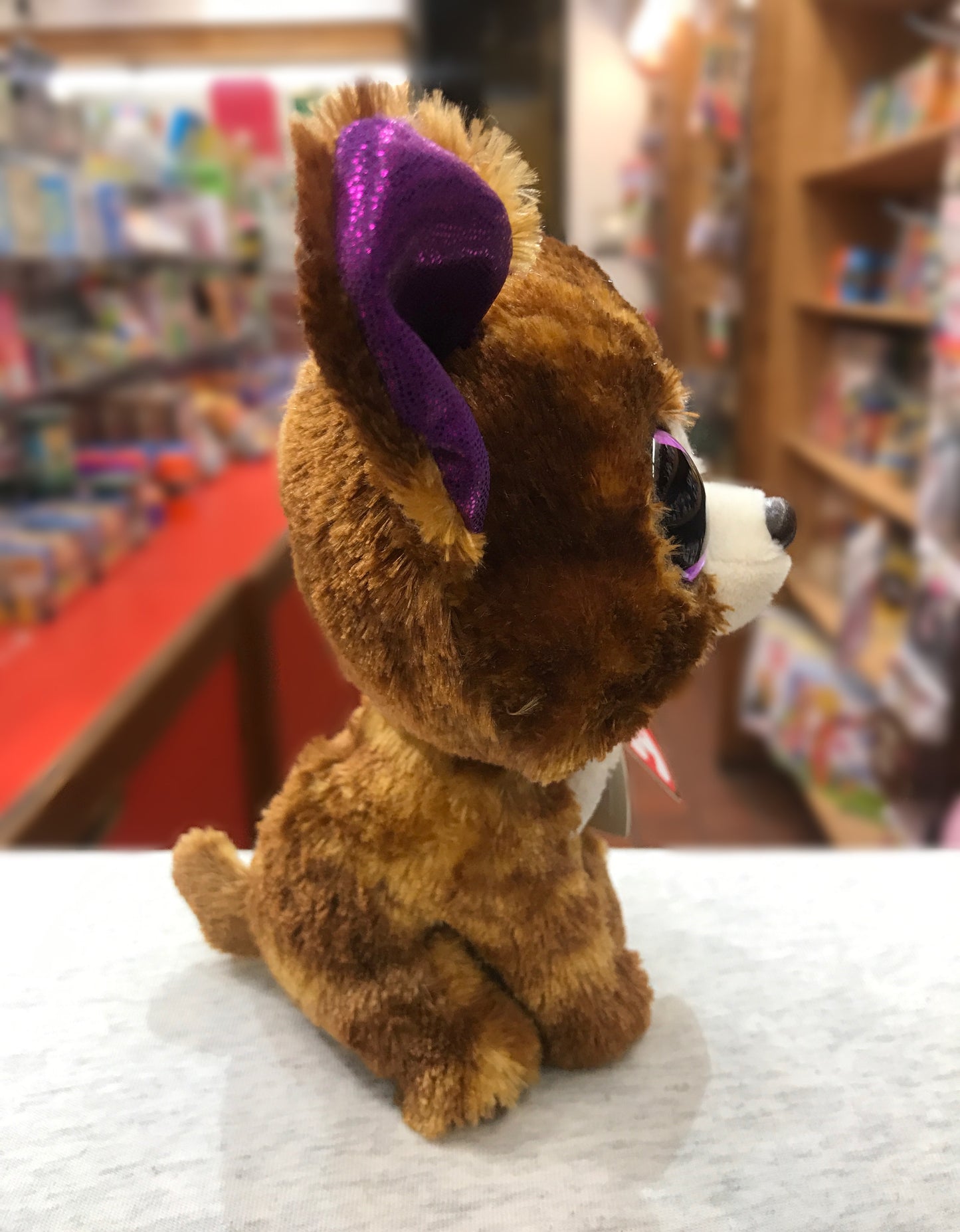 Ty Beanie Boo Dexter Dog plush toy with brown fur and purple sparkly ears, sitting in a toy store display