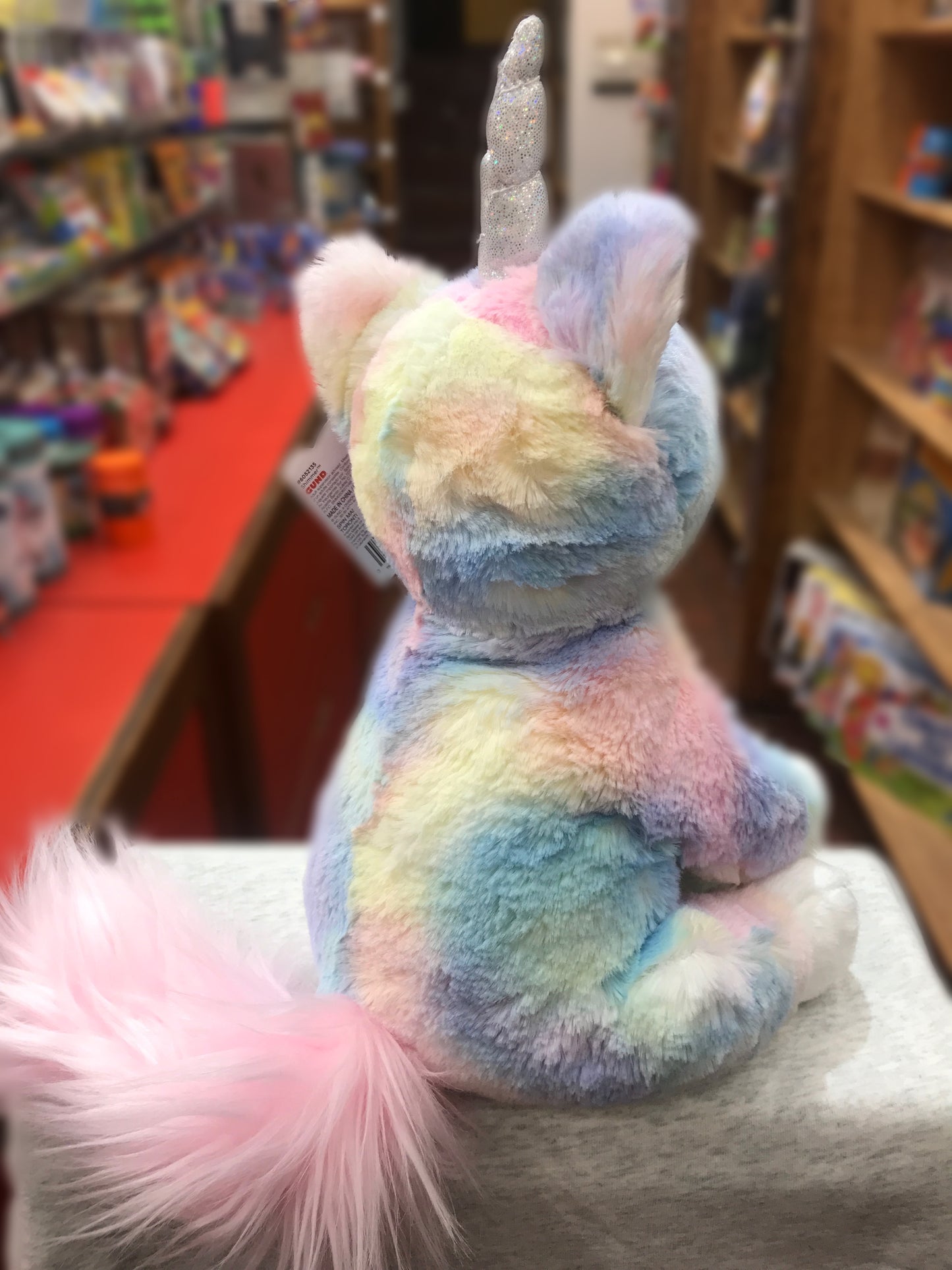 Gund Shimmer Caticorn plush toy with pastel fur, silver horn, and pink tail, displayed in a store setting