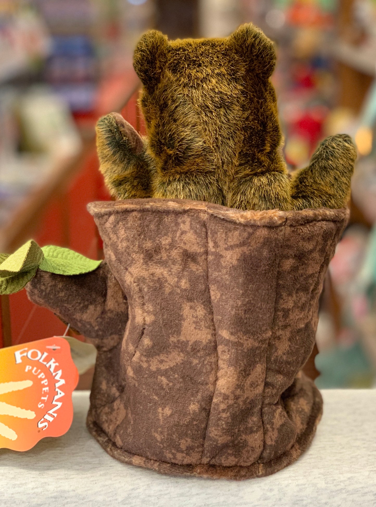 Folkmanis bear hand puppet peeking from plush tree stump, soft brown fur, movable arms, orange tag visible