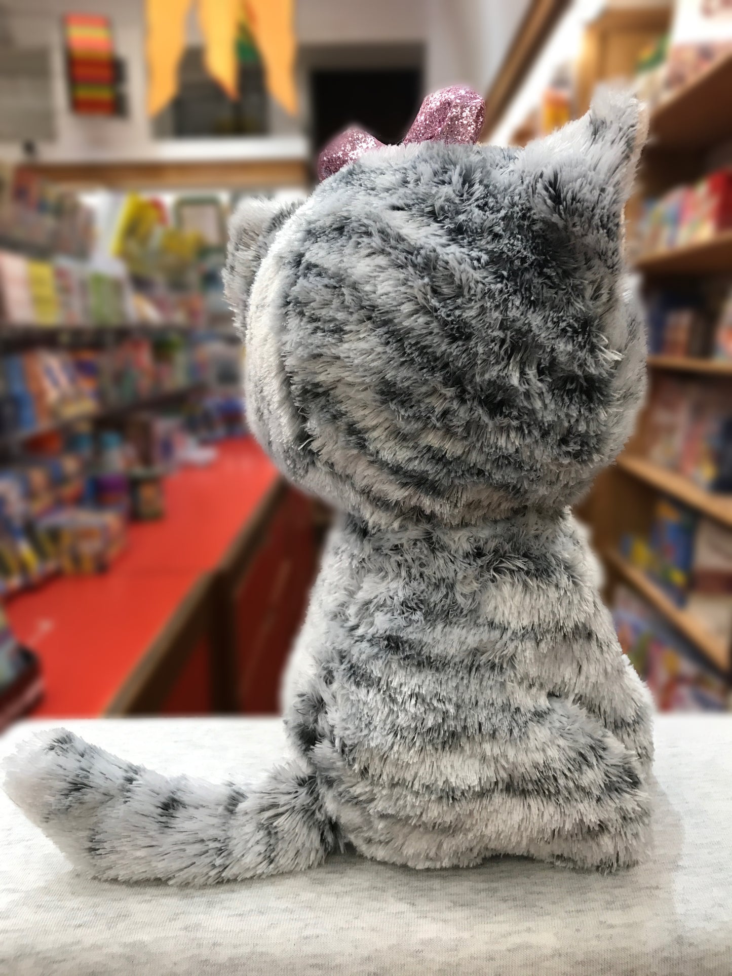 Ty Beanie Boo Kiki Kitty plush toy sitting in bookstore, showing soft gray fur and pink sparkly ears
