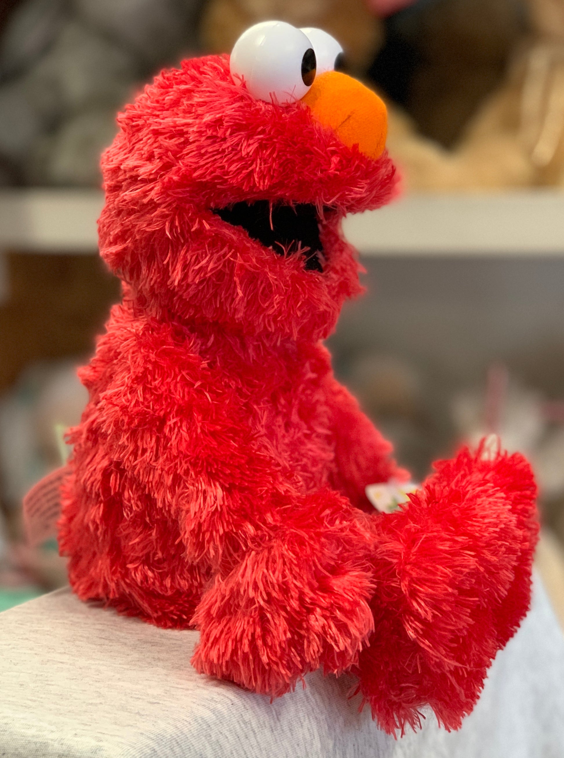 Gund Sesame Street Elmo plush toy, 13 inches tall, soft red fur, sitting on surface, close-up view