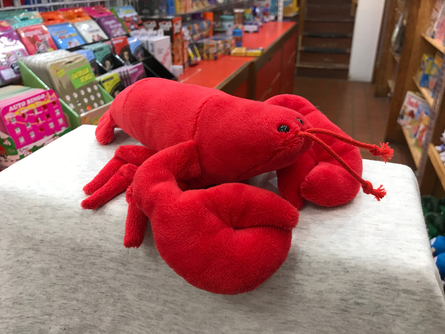 Bright red plush lobster toy with large claws and antennae, displayed in a toy store among other children's products
