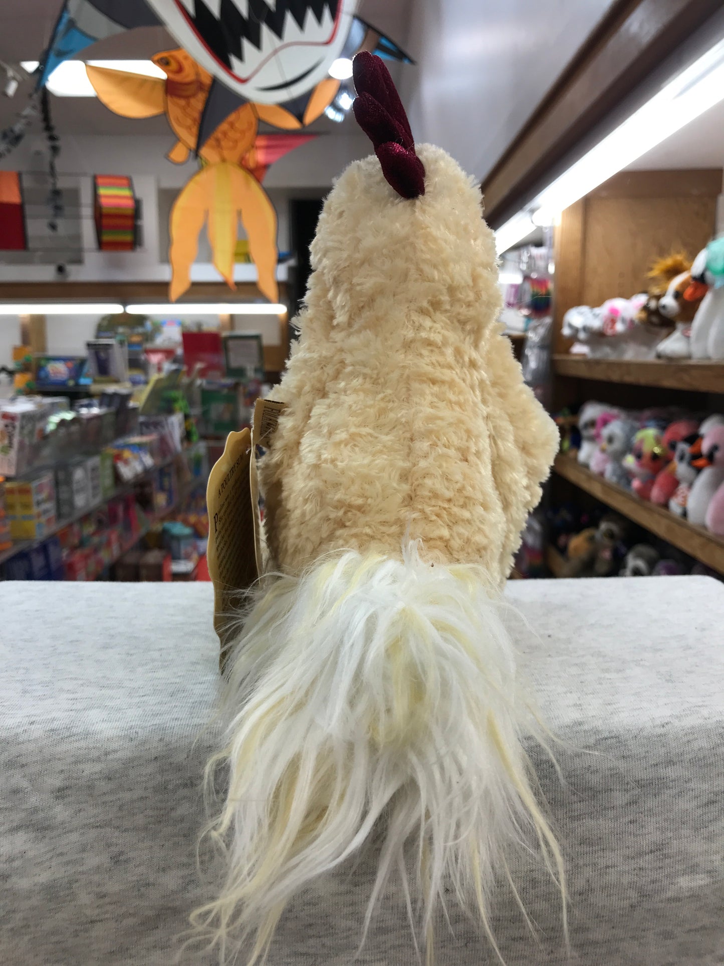 Plush Folkmanis funky chicken puppet with soft feathers and red comb, displayed in toy store with colorful decorations
