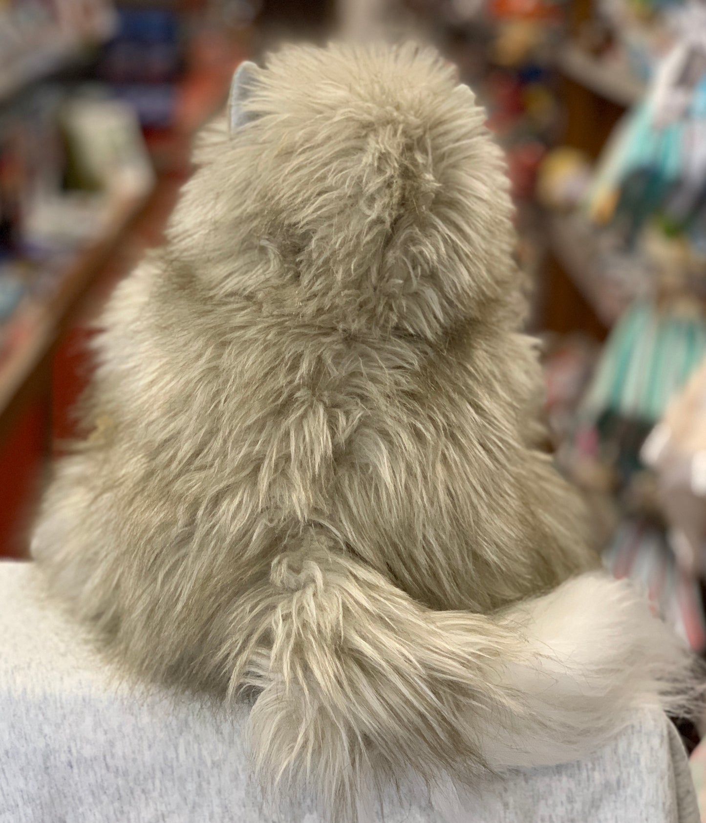 Fluffy cat hand puppet with long luxurious fur and tail, shown from behind in a toy store setting