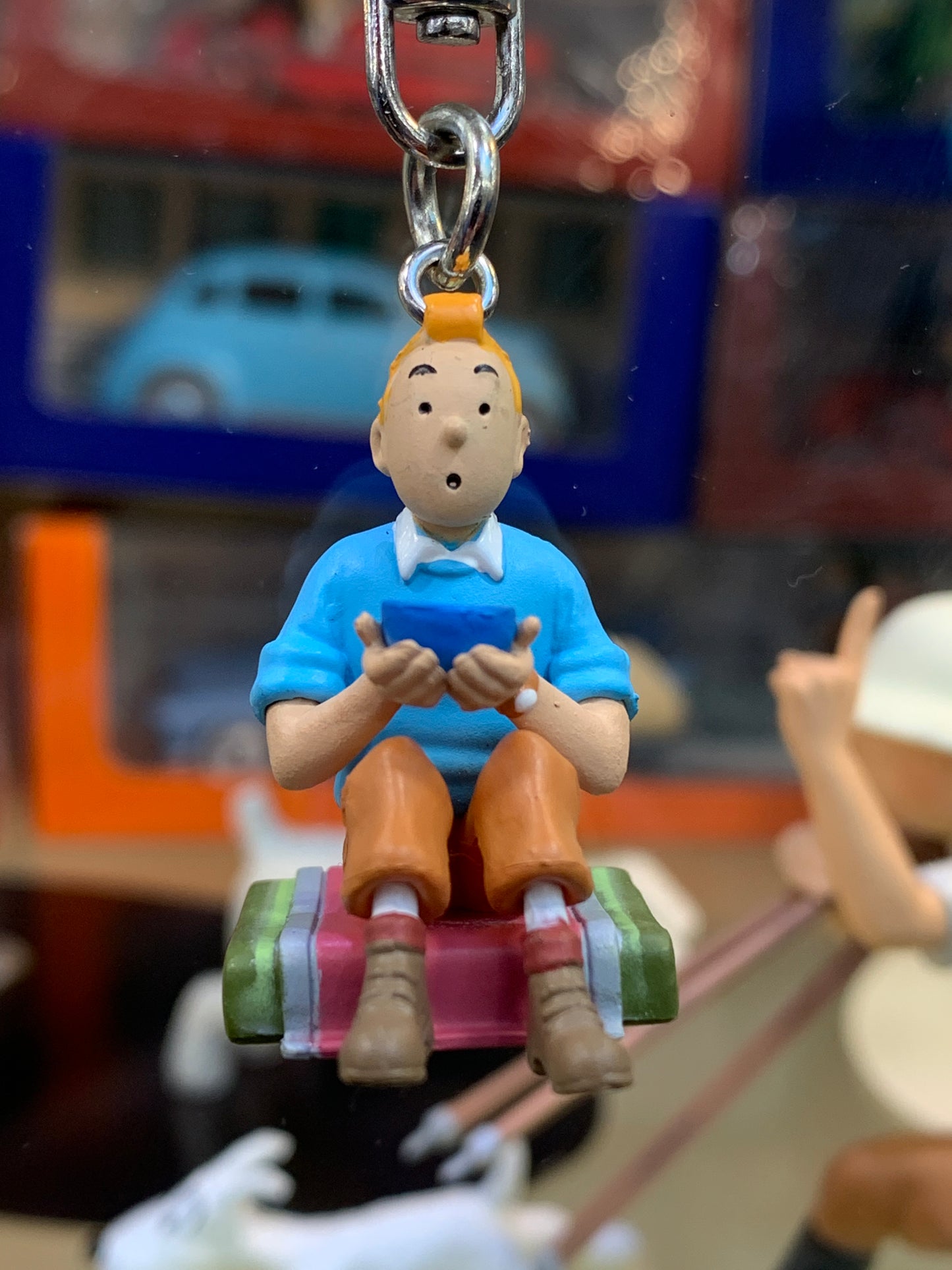 Tintin in Tibet keychain figure, seated with blue shirt and orange pants, holding blue object, 3.8cm tall mini collectible
