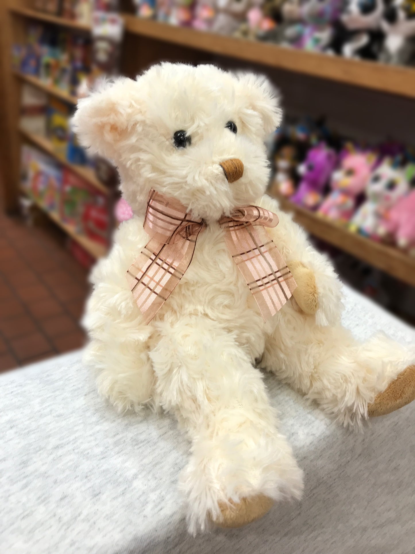 Cream fuzzy teddy bear plush with pink bow, soft and cuddly 6-inch stuffed animal on display in toy store