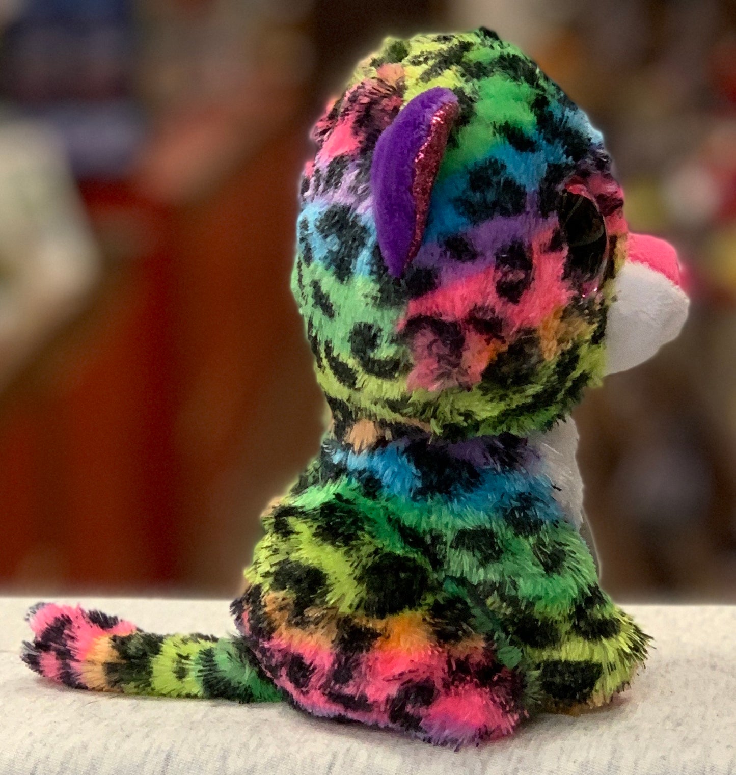 Colorful Ty Beanie Boo Dotty Leopard plush toy with vibrant rainbow spots and sparkling purple ears, seen from behind