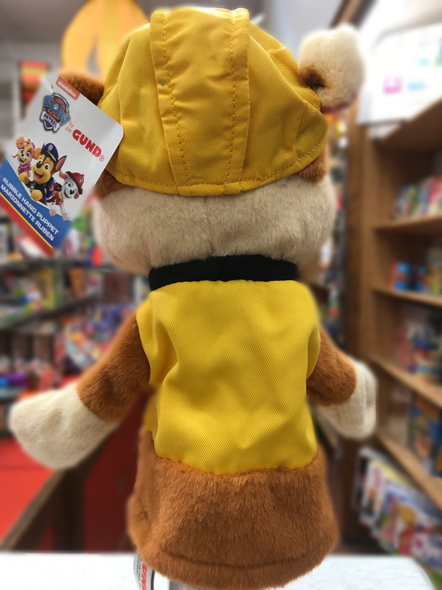 Gund Paw Patrol Rubble hand puppet, soft plush toy in yellow construction uniform, viewed from behind in toy store