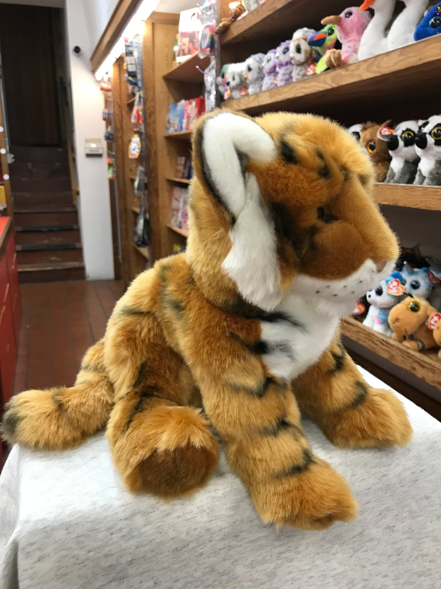 Soft and cuddly Bengal tiger cub plush toy with realistic orange and white fur, displayed in a toy store with other stuffed animals