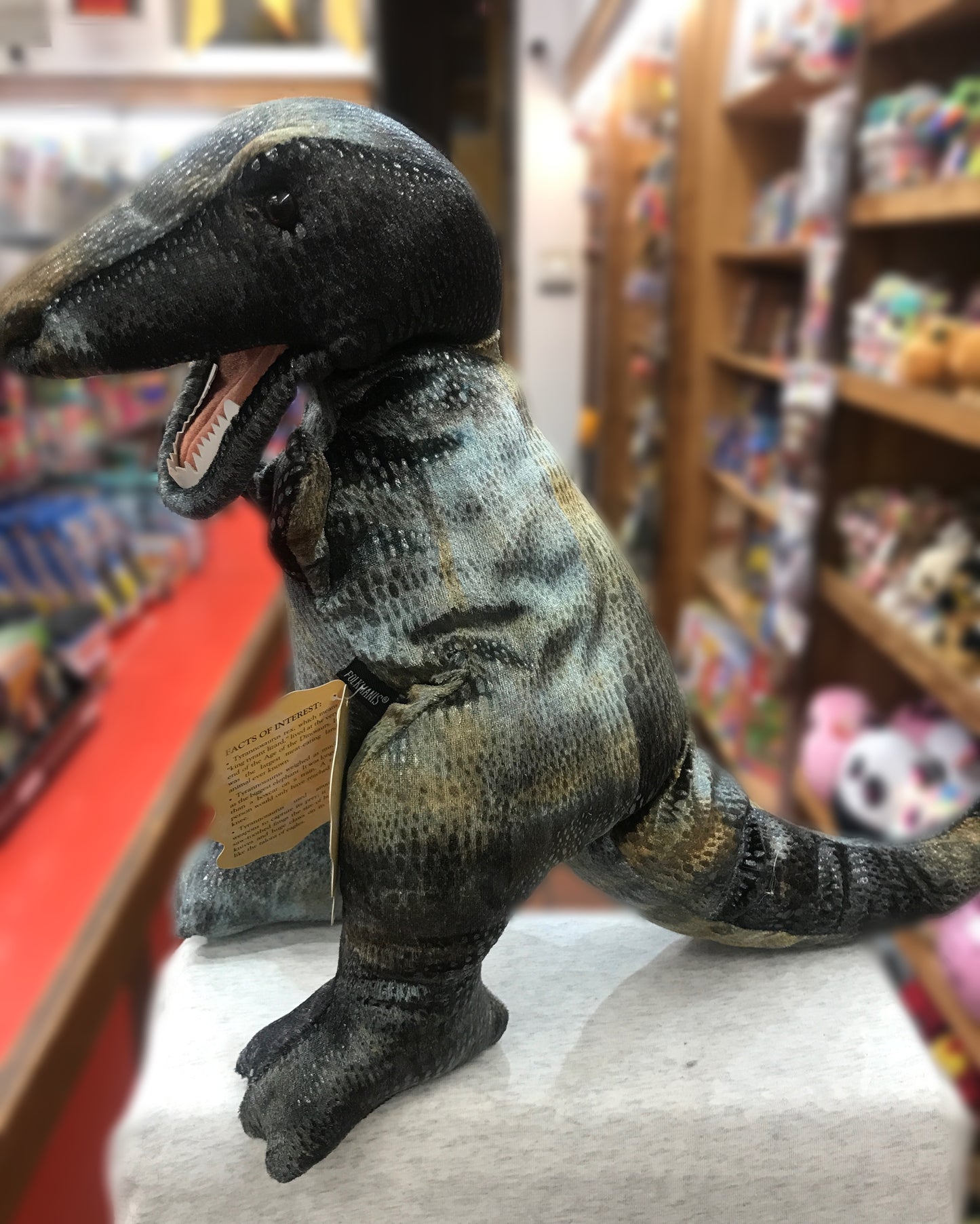 Realistic Folkmanis Tyrannosaurus Rex puppet with open jaws, displayed in toy store among shelves of other toys