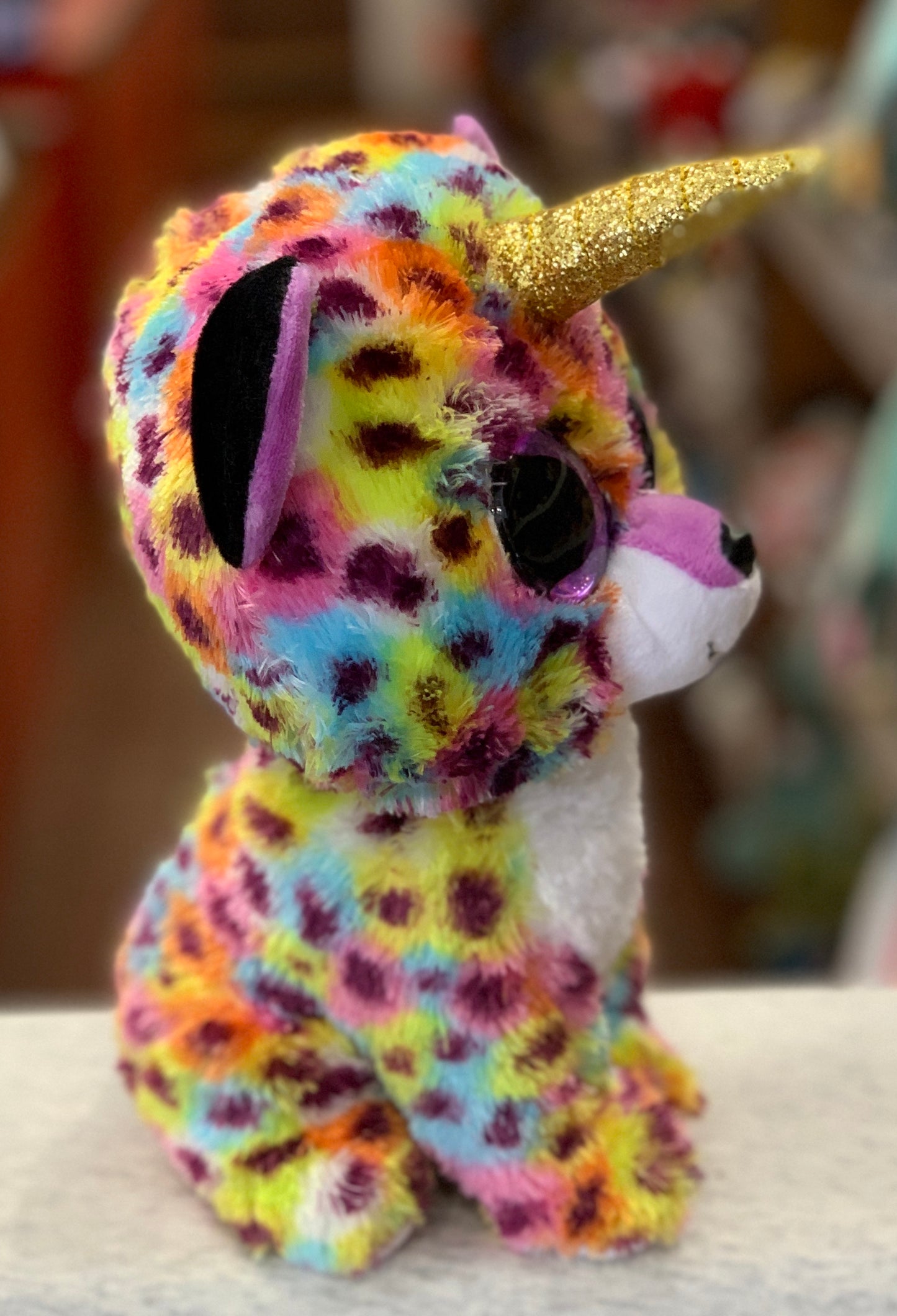 Colorful Ty Beanie Boo unicorn plush toy with sparkly gold horn and multicolored spotted fur, featuring large purple eyes
