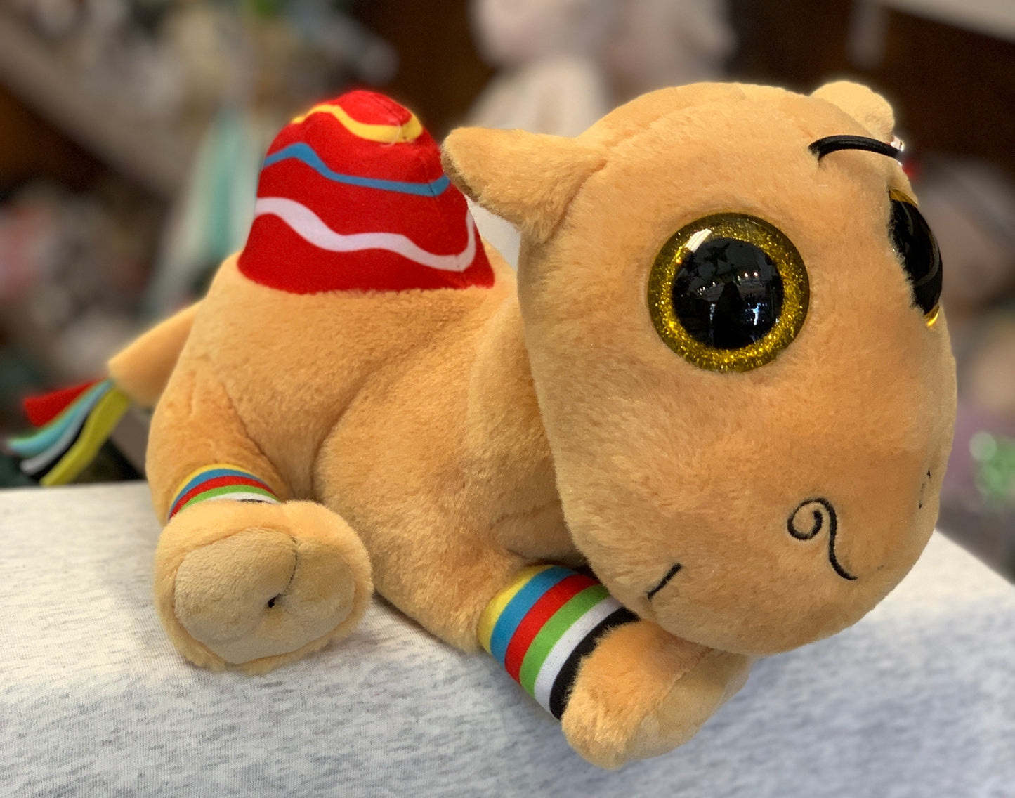 Ty Beanie Boo Jamal Camel plush toy with bright gold eyes, colorful striped accessories, and smiling face on display