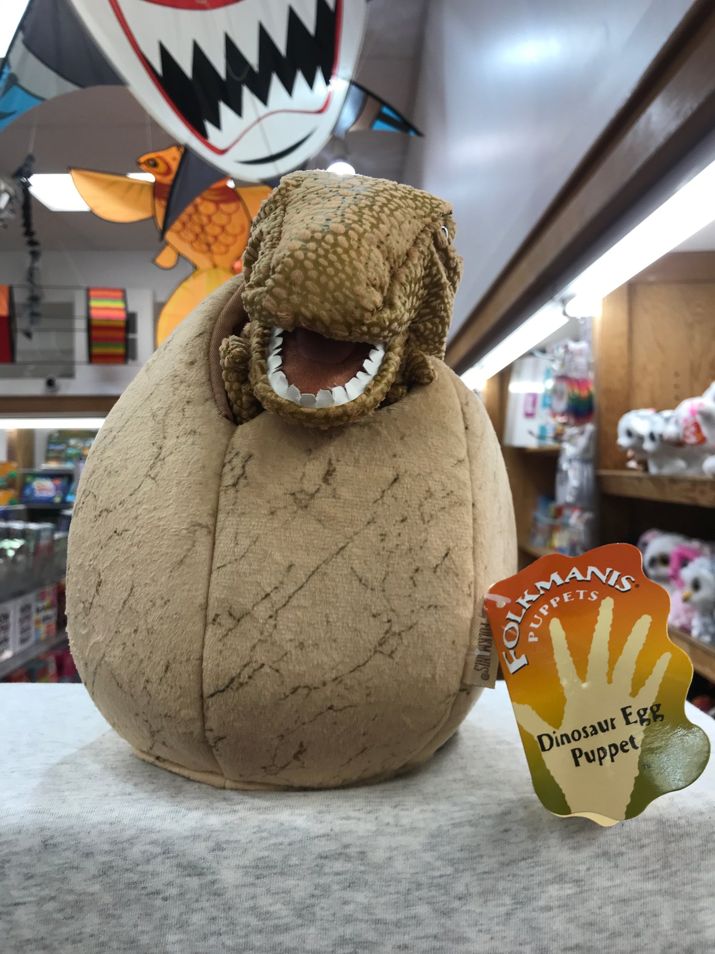 Folkmanis Dinosaur Egg Puppet with baby T-Rex peeking out, displayed in toy store with product tag visible