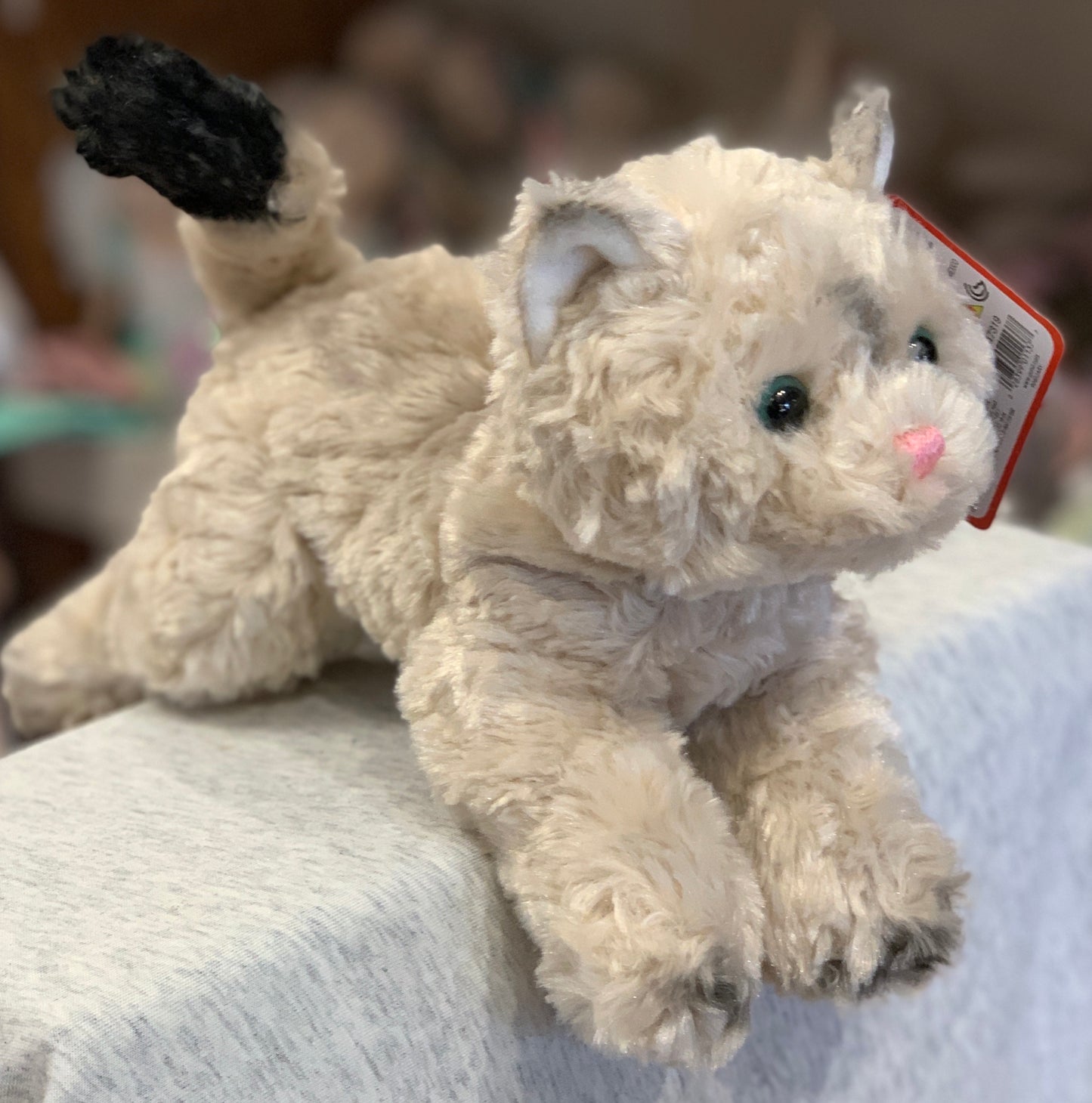 Gund Bootsie tan cat plush toy with fluffy fur, green eyes, and black-tipped tail, displayed on light fabric