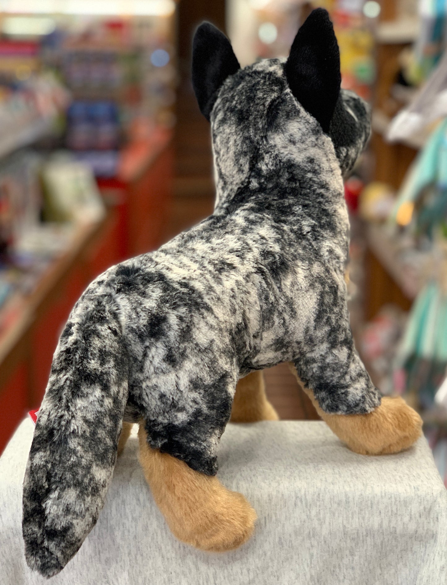 Realistic Australian Cattle Dog plush toy with blue merle coat and tan paws, standing alert in a toy store setting