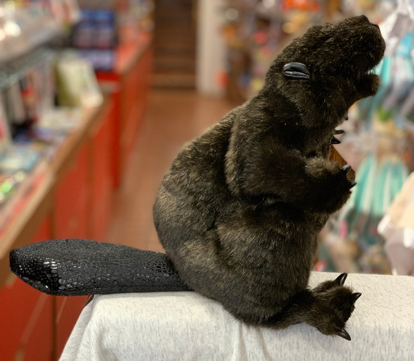 Realistic Folkmanis beaver puppet with brown fur, open mouth, and textured tail, displayed in a toy store setting