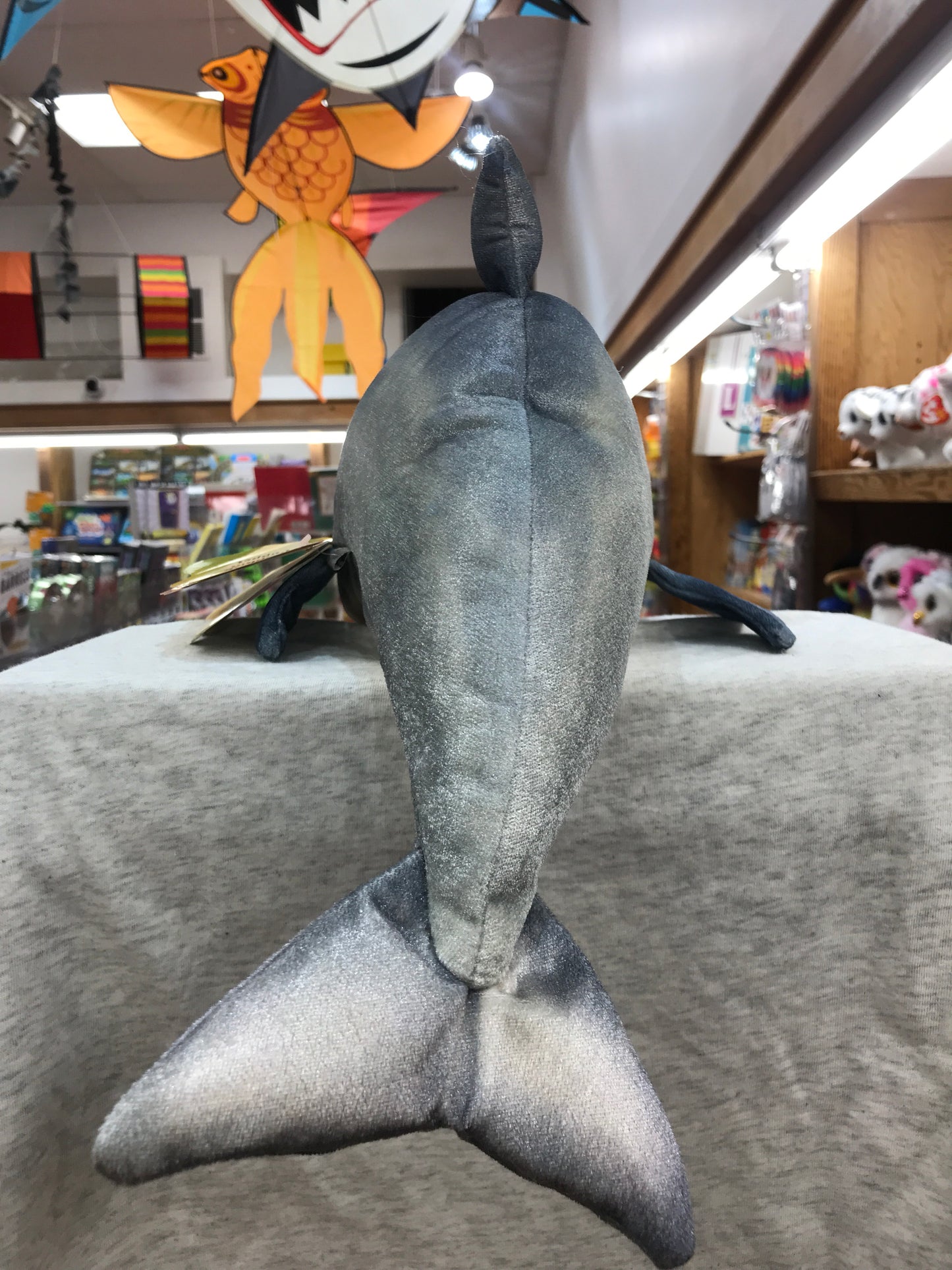 Folkmanis whistling dolphin puppet displayed in toy store, gray plush body with movable fins, tail raised vertically
