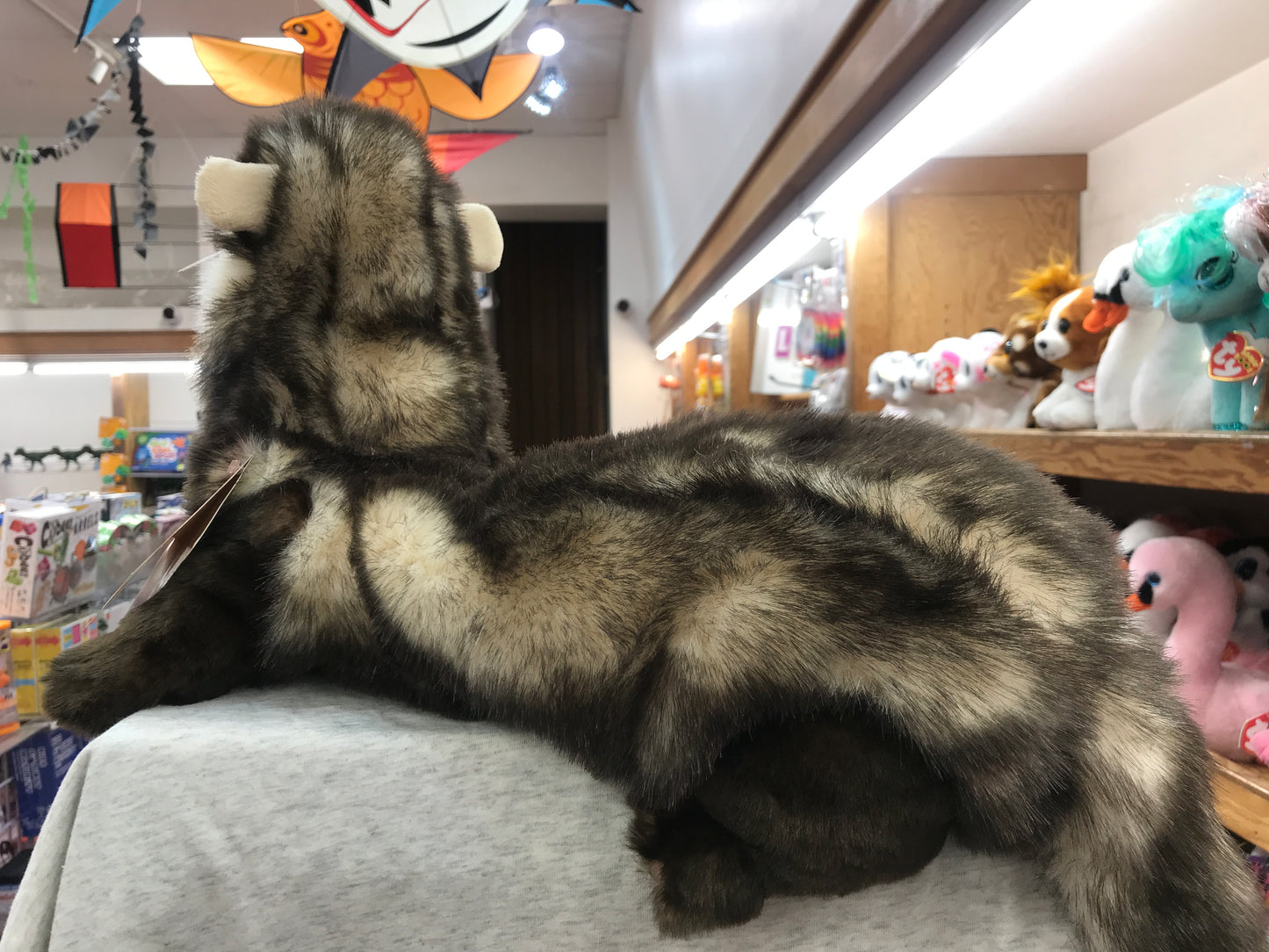 Realistic Folkmanis ferret puppet with soft fur displayed in toy store, surrounded by other plush animals and toys