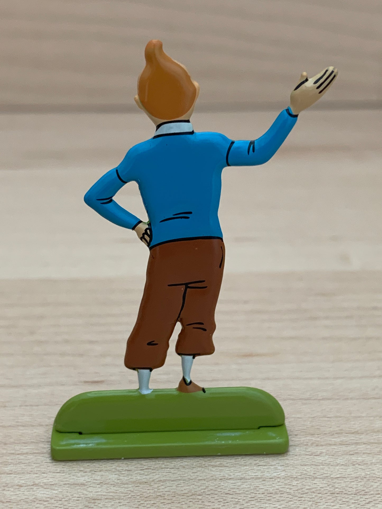 Welcoming Tintin metal relief figure, back view, waving hand, blue sweater, brown pants, on green base, 5.5cm tall collectible