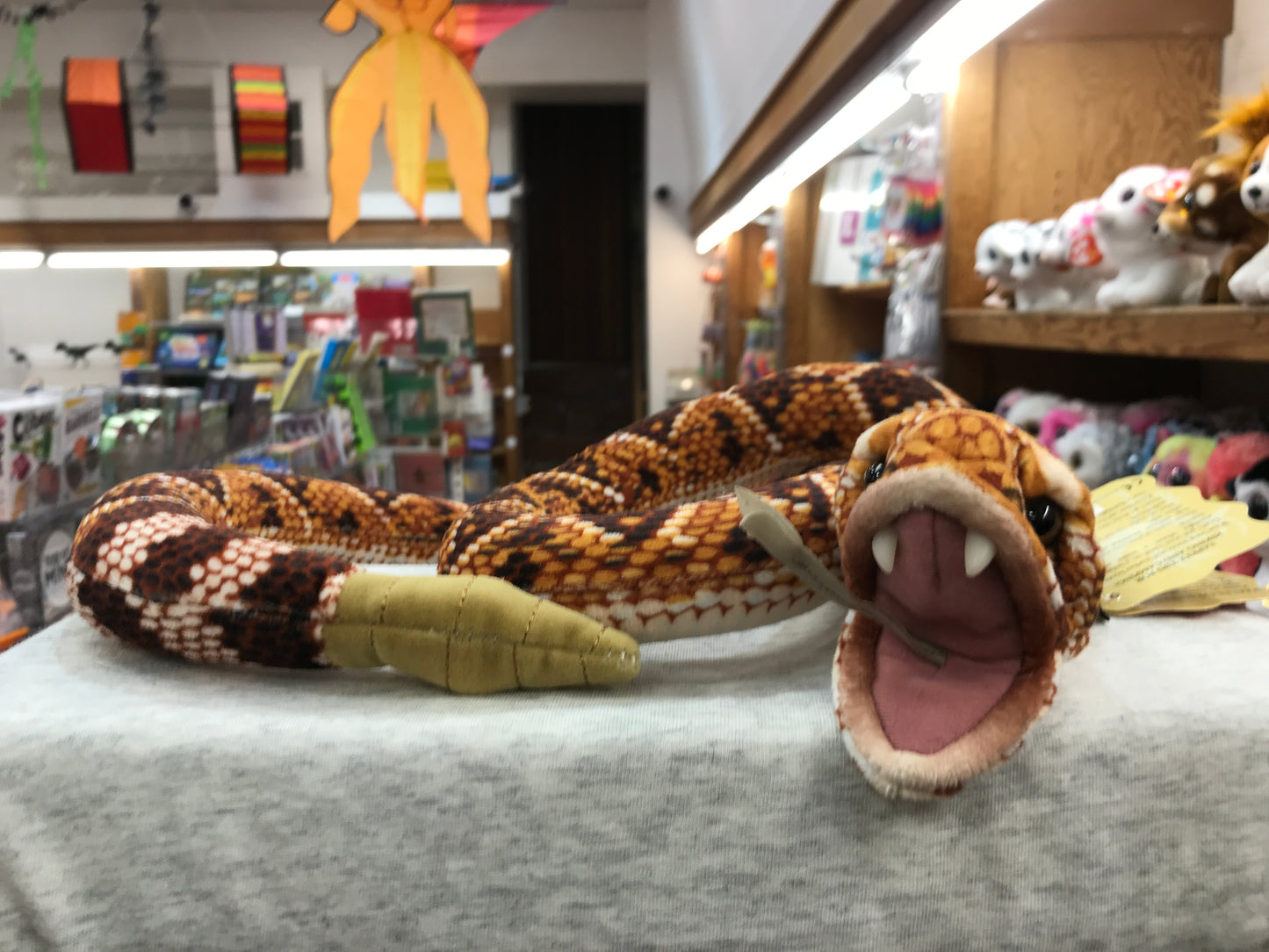Realistic Folkmanis rattlesnake puppet with open mouth and rattle tail, displayed in toy store with other plush animals