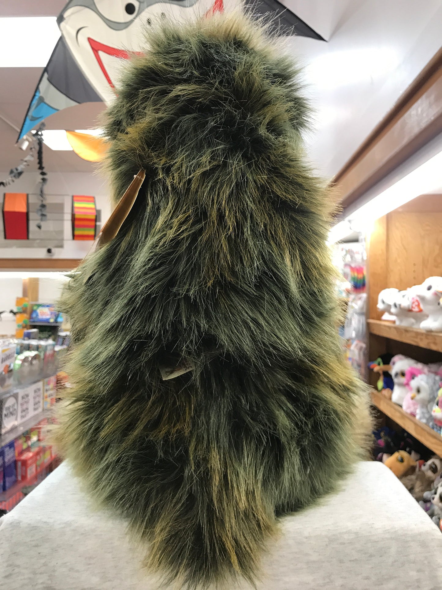 Realistic Folkmanis three-toed sloth puppet with lifelike fur, shown in toy store setting surrounded by other stuffed animals