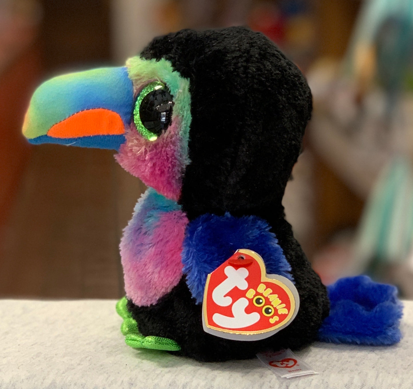 Colorful Ty Beanie Boo Beaks bird plush toy with large green eyes, rainbow beak, and black body, displaying Ty heart tag