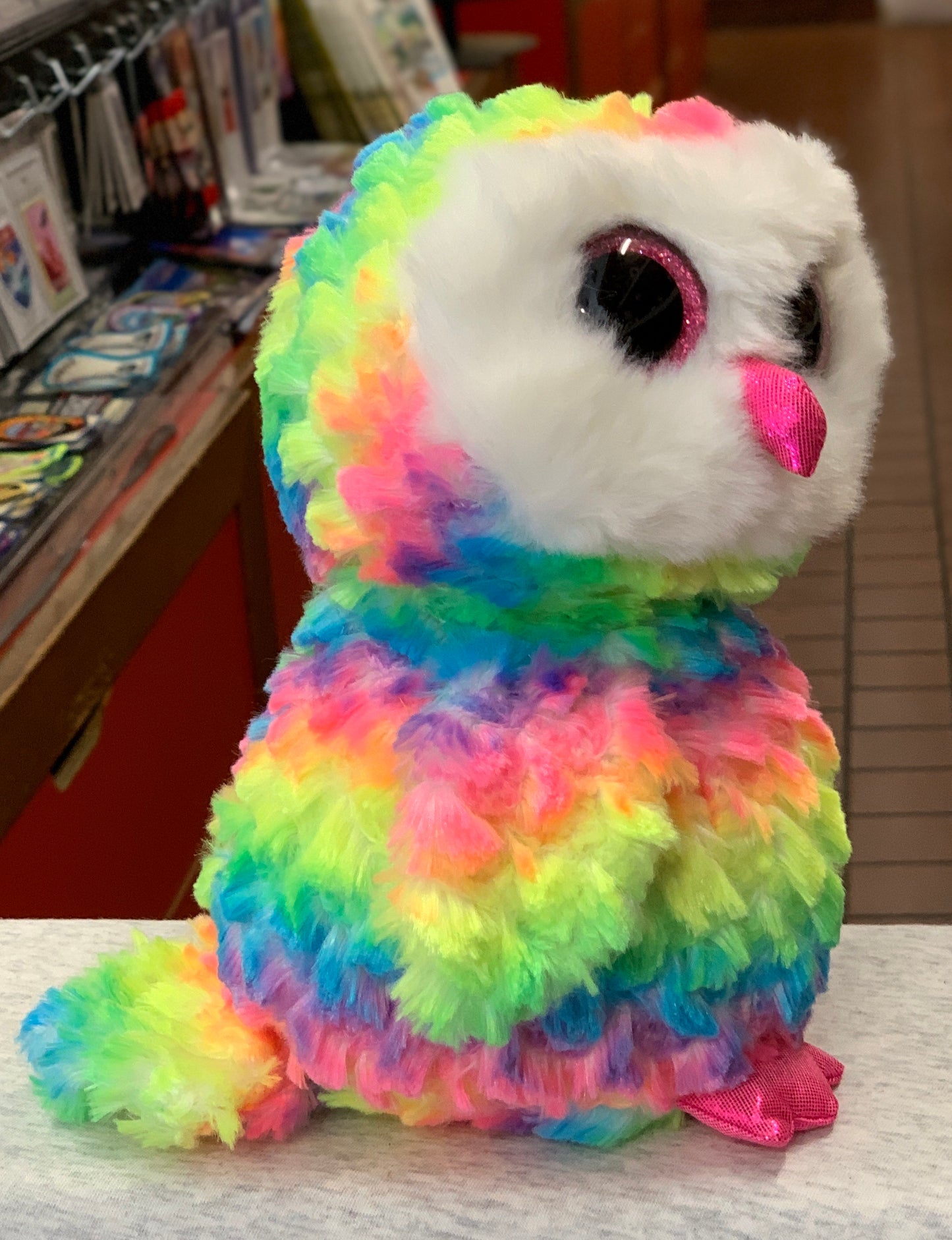 Colorful rainbow Ty Beanie Baby Owen Owl plush with large sparkly eyes and pink beak, sitting on display shelf