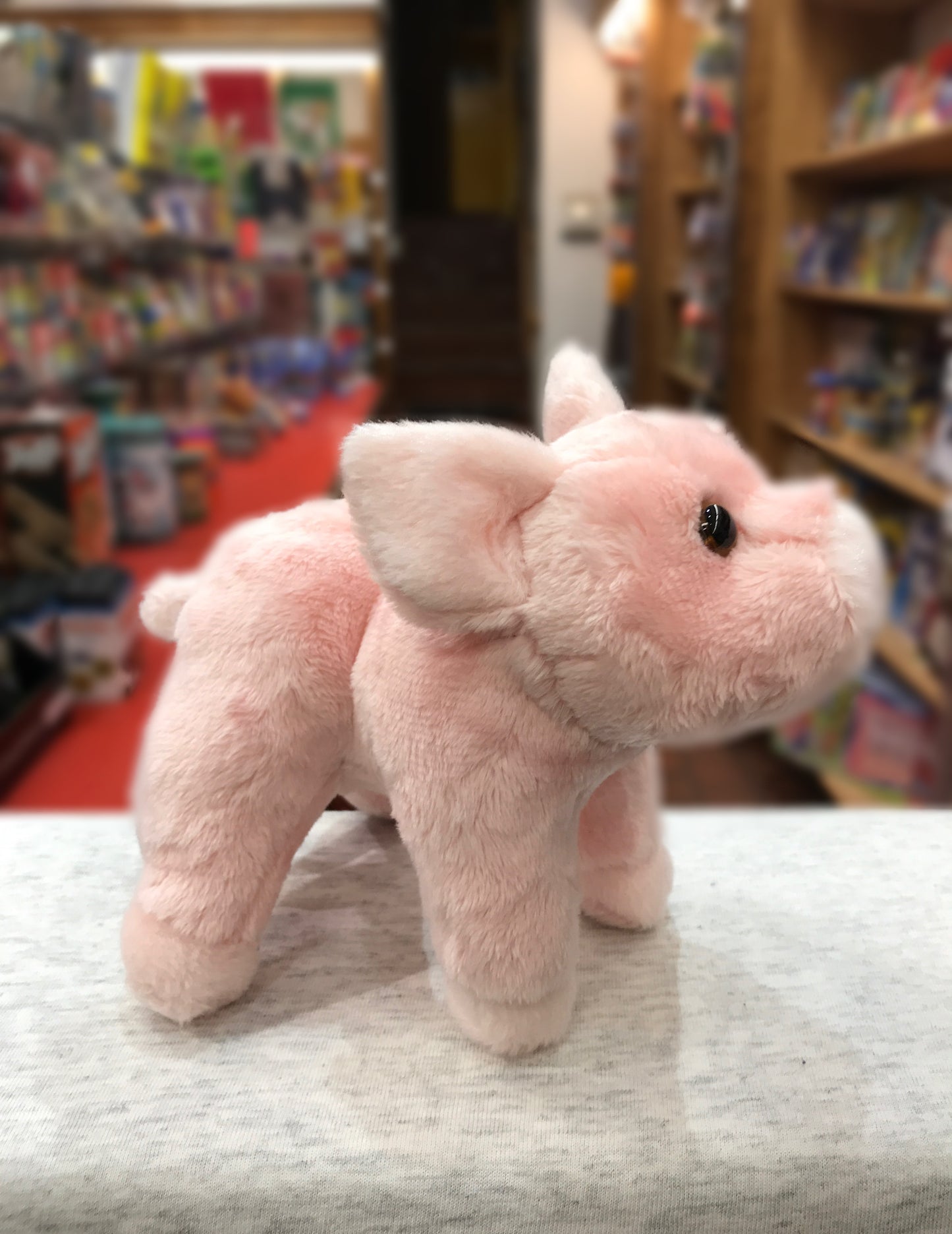 Adorable pink pig plush toy, Buttons, standing on display in a toy store with bookshelves in background